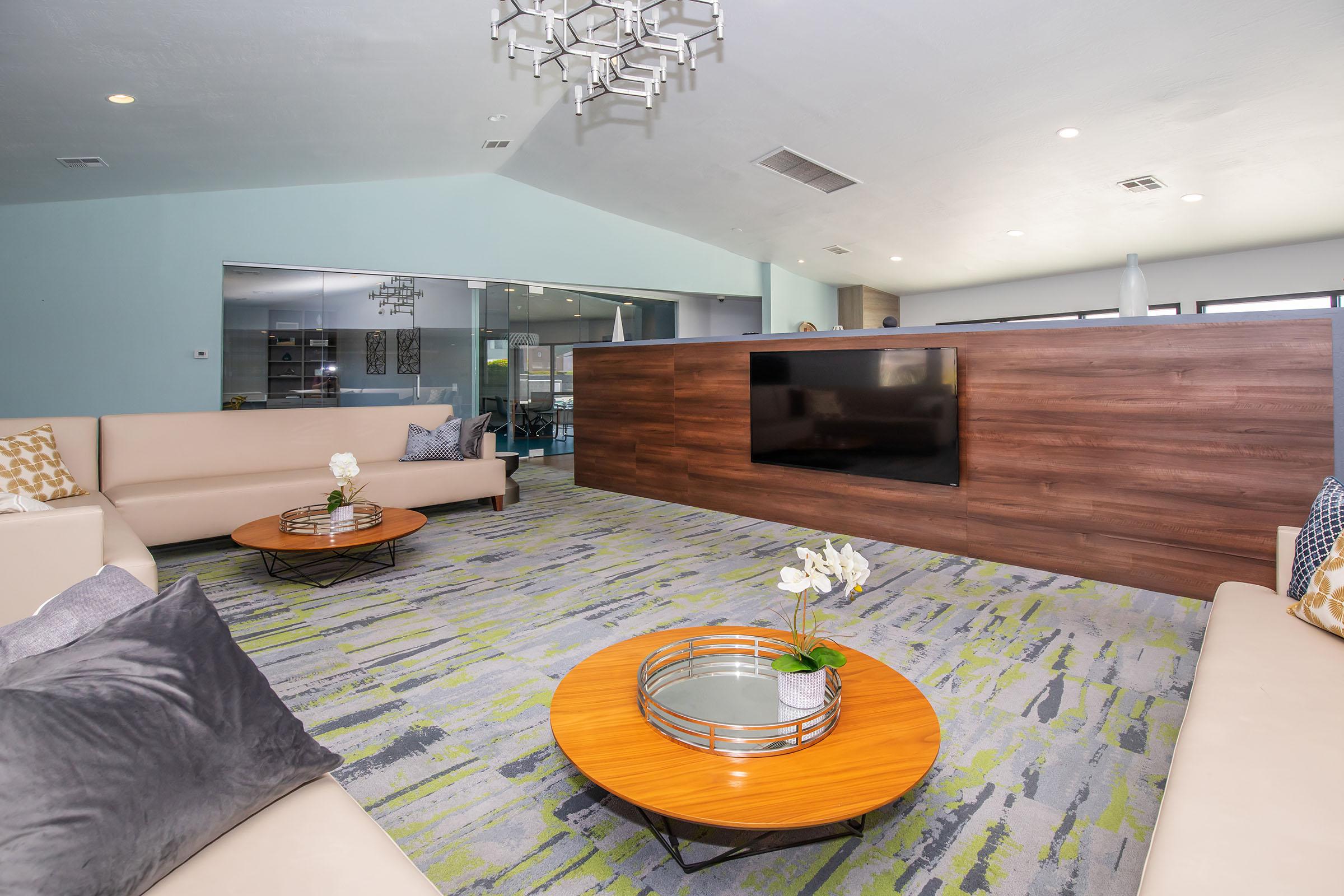 Modern indoor clubhouse with large sectional couch, round coffee tables, and a flat screen TV at Rise at the District apartments