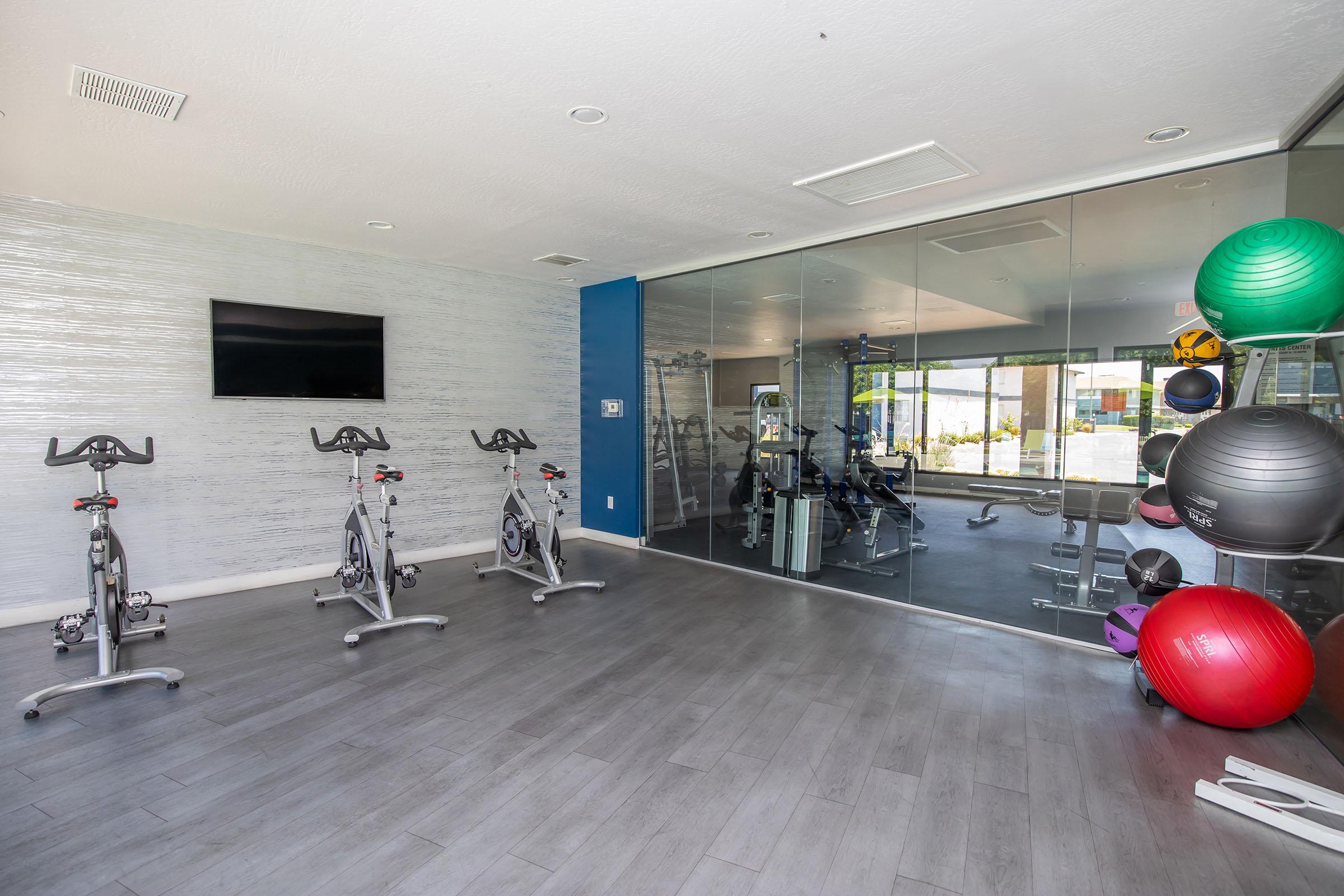 Rise at the District apartments indoor fitness center with work out balls and bikes facing a wall of mirrors and a flat screen TV