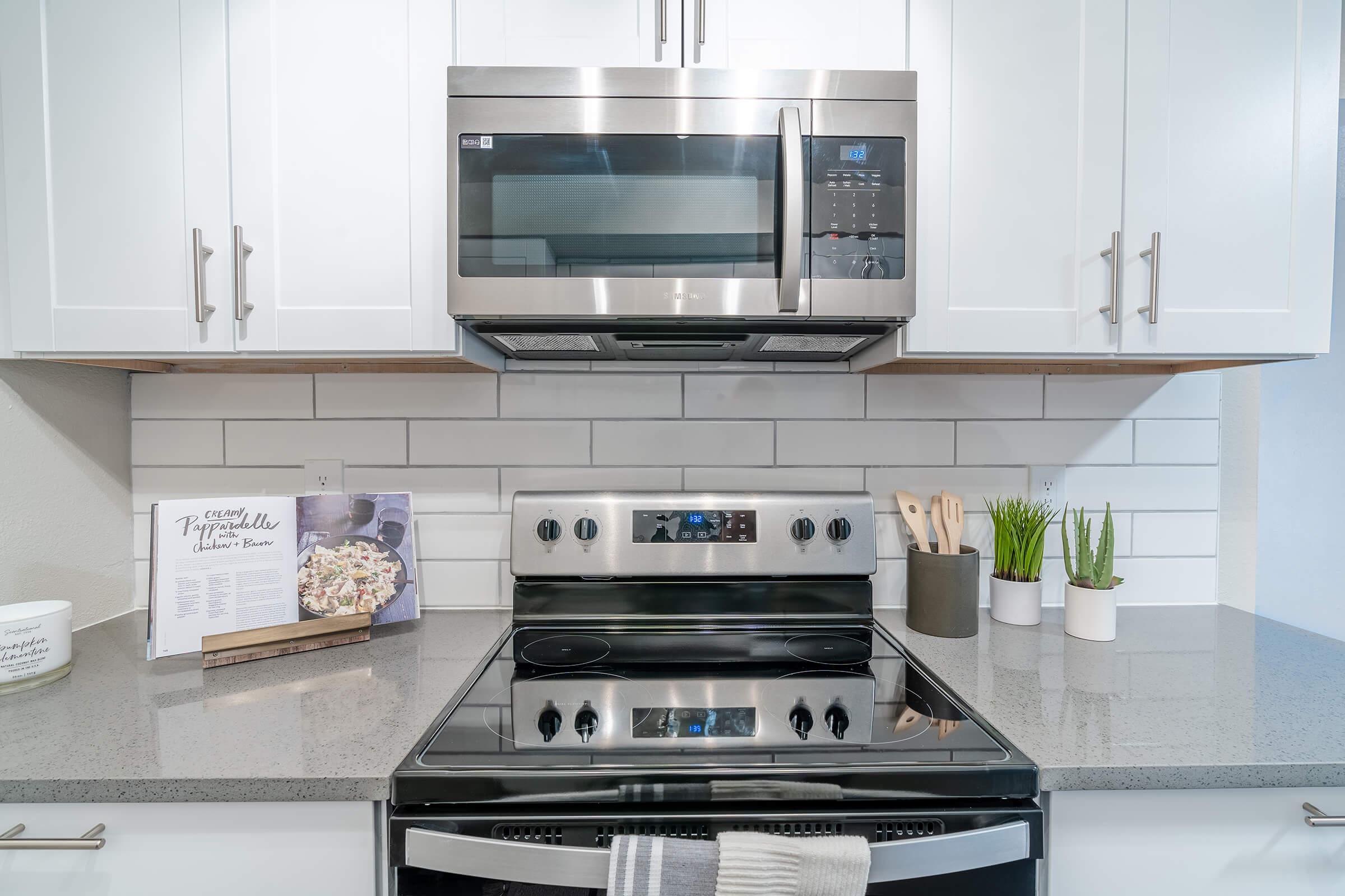 Close up of stainless steel stove top and microwave next to grey quartz countertops