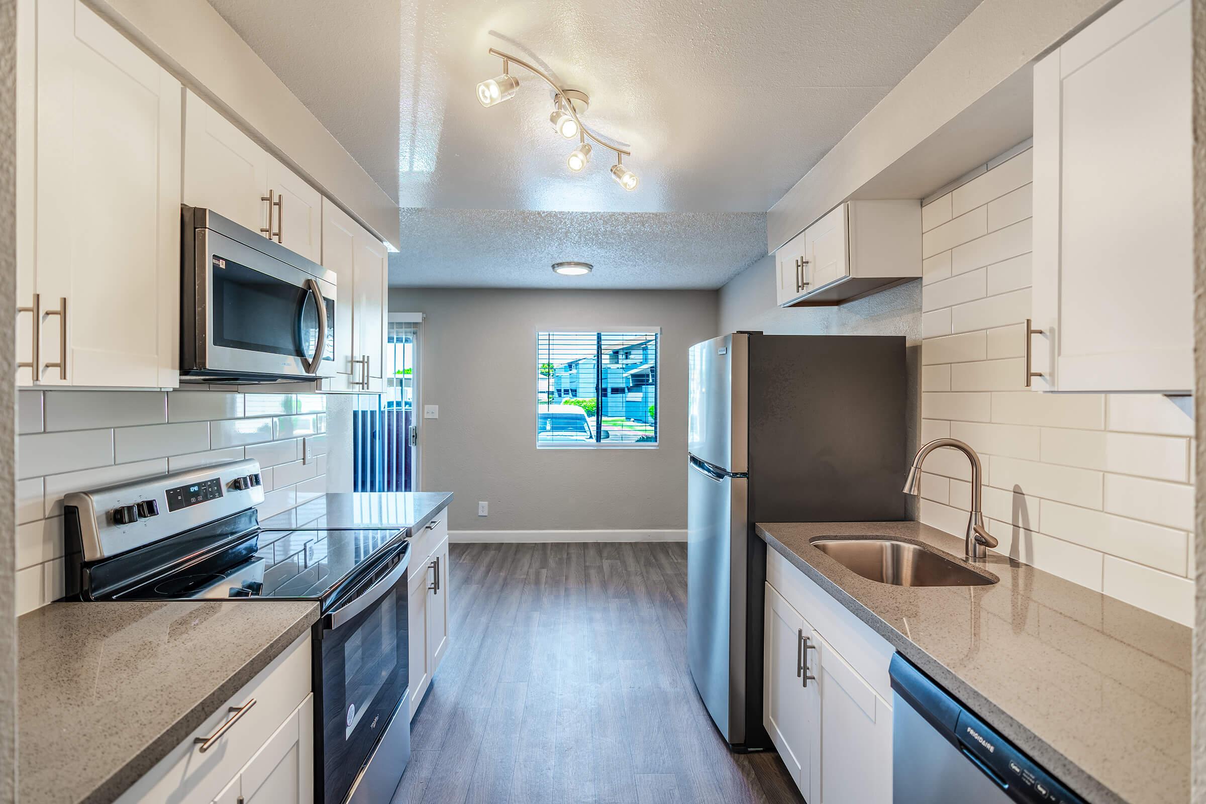 Galley way renovated kitchen with white cabinets, stainless steel appliances and white back splash