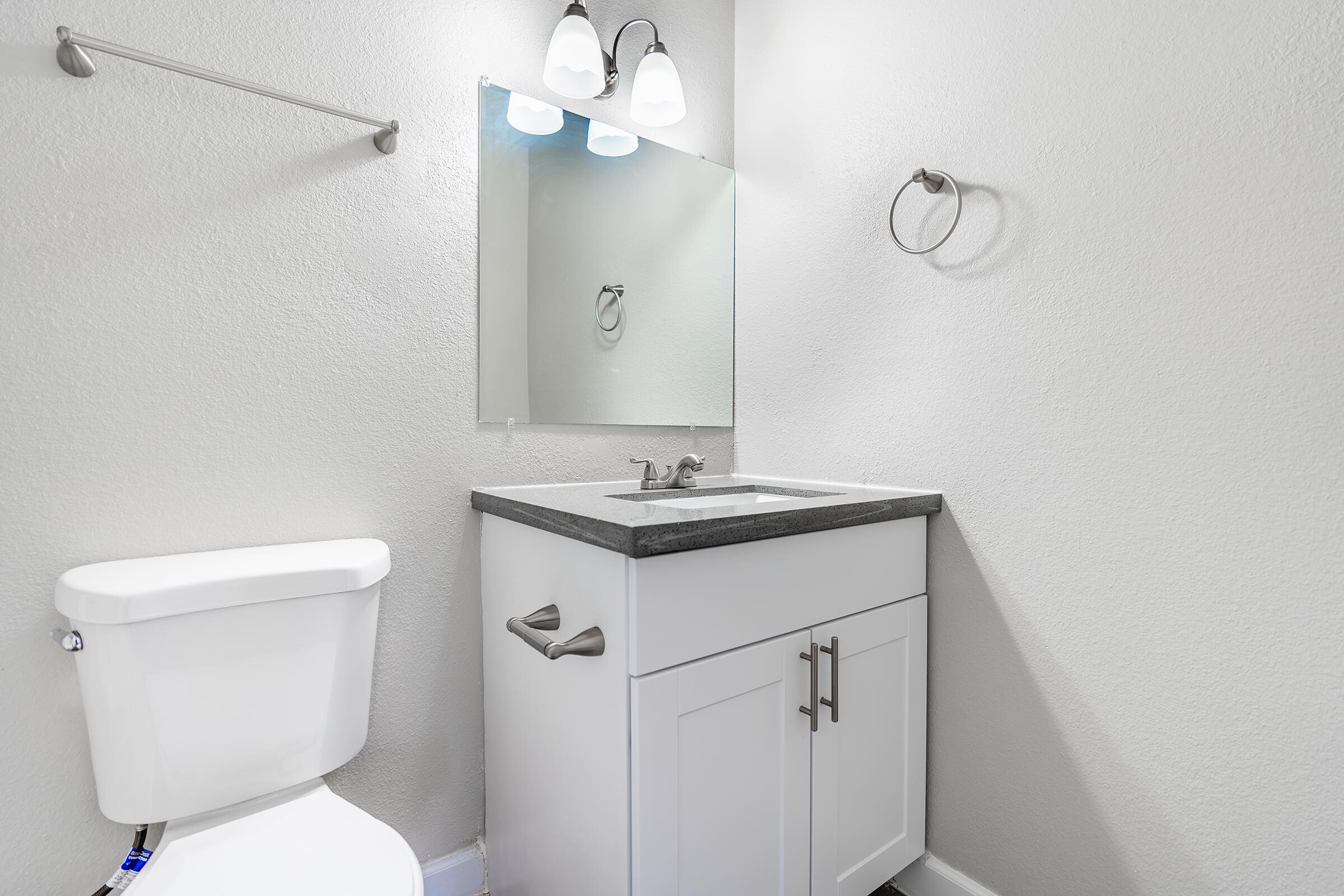 White cabinet vanity with mirror and toilet next to it
