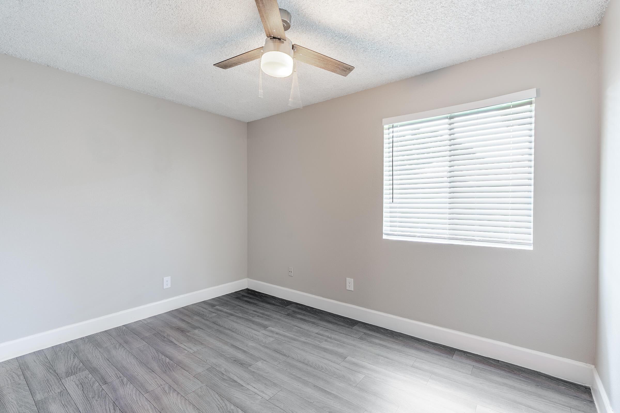 Modern bedroom with wood flooring, a large window, and a ceiling fan