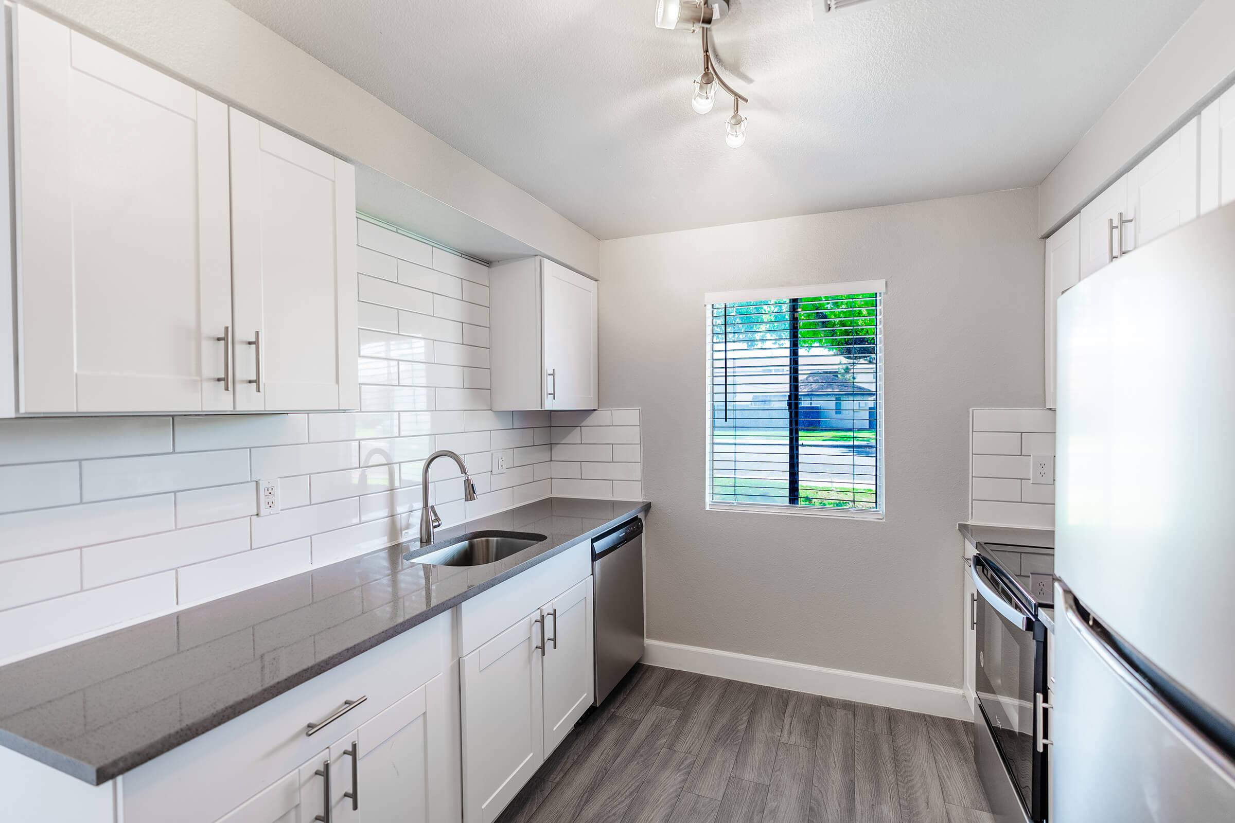 Galley way kitchen with small window, white cabinets, and  quartz countertops