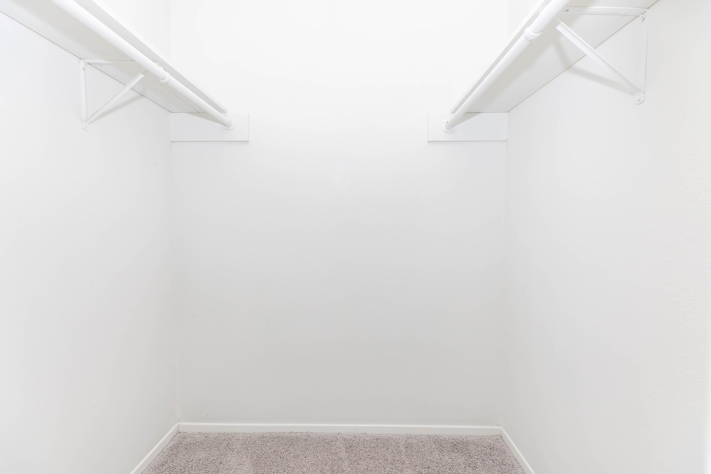 Empty closet space with white walls and two horizontal shelves. The floor is covered with a plush, light-colored carpet, creating a clean and minimalist look.