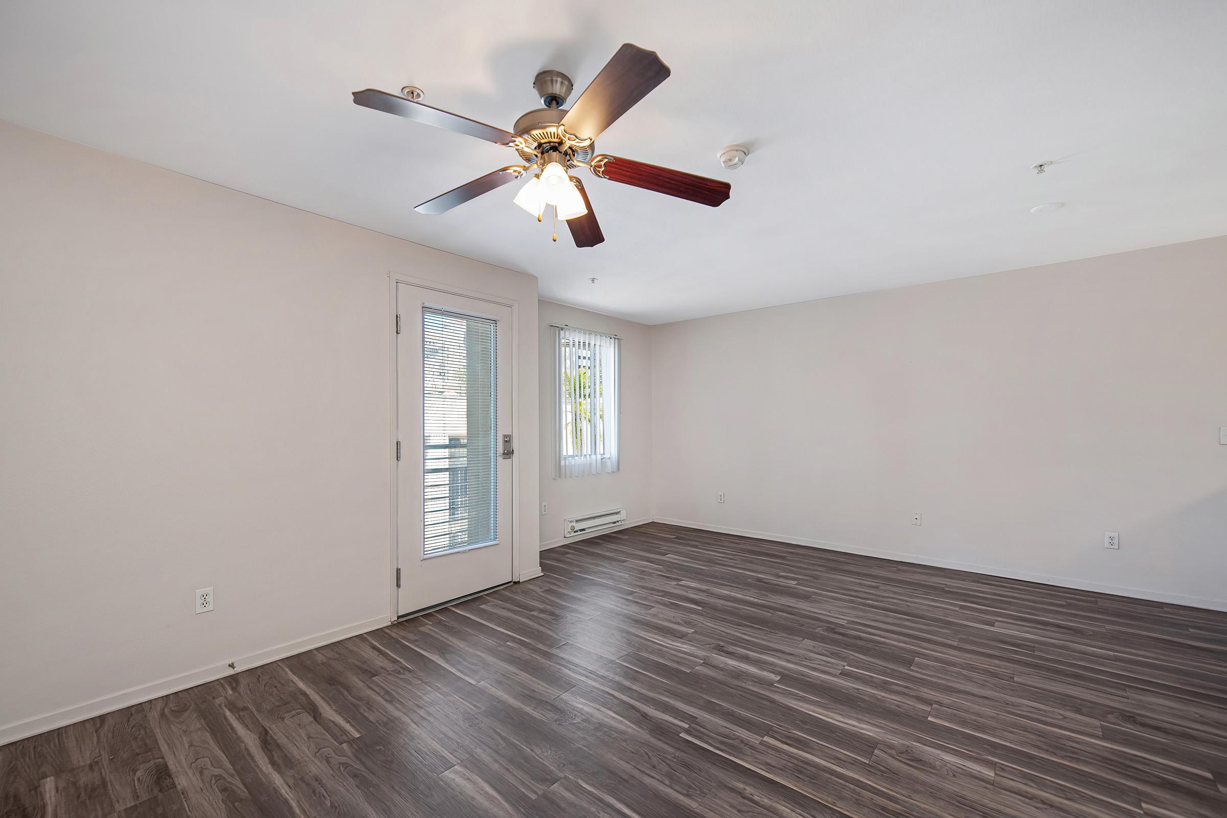 Spacious, light-filled room featuring a ceiling fan, wood-style flooring, and sliding glass door leading to a patio. The walls are painted in soft neutral tones, enhancing the airy ambiance. Ideal for living or dining space.