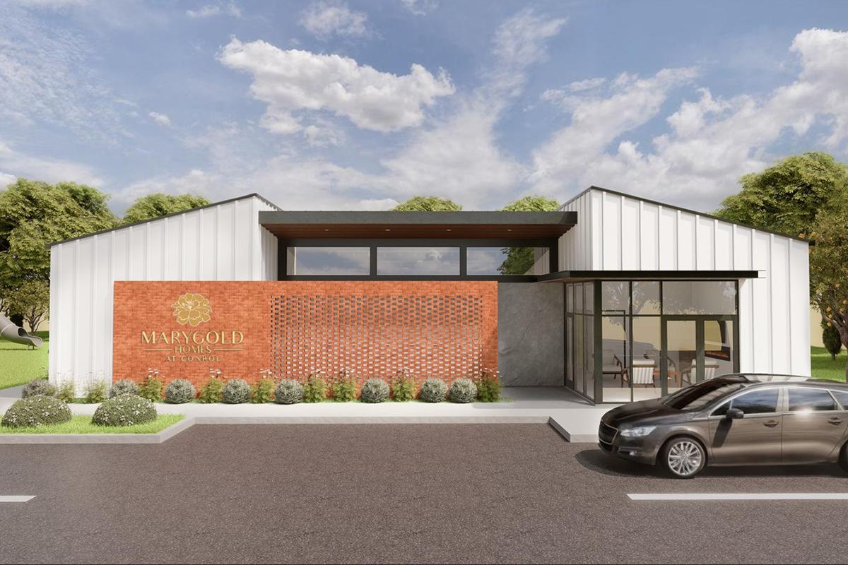 A modern building facade featuring a combination of red brick and white siding. The structure includes large windows and a welcoming entrance. The name "Marygold Home" is prominently displayed on the front, surrounded by landscaped greenery and a parked car in the foreground under a partly cloudy sky.