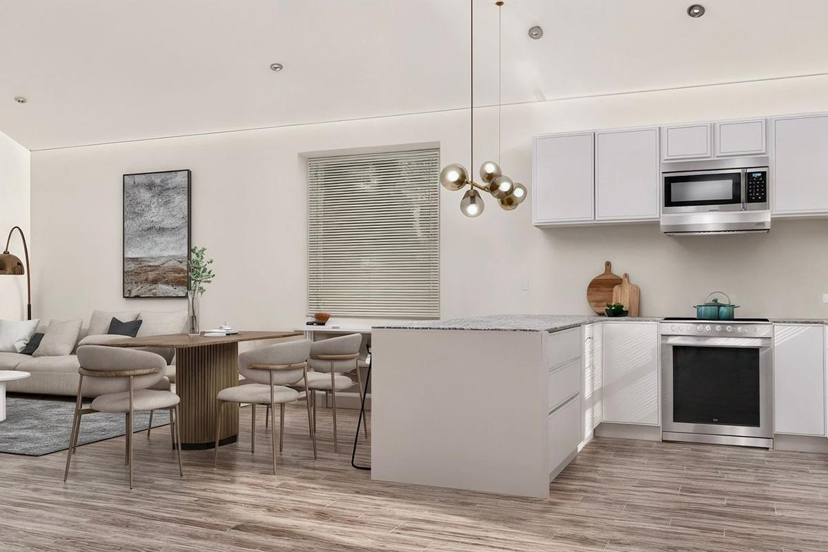 Modern kitchen and dining area featuring a sleek white cabinetry, a central island with a gray countertop, a dining table with stylish chairs, and a comfortable living space with a cozy couch. Natural light brightens the room, complemented by minimalist decor and stainless steel appliances.