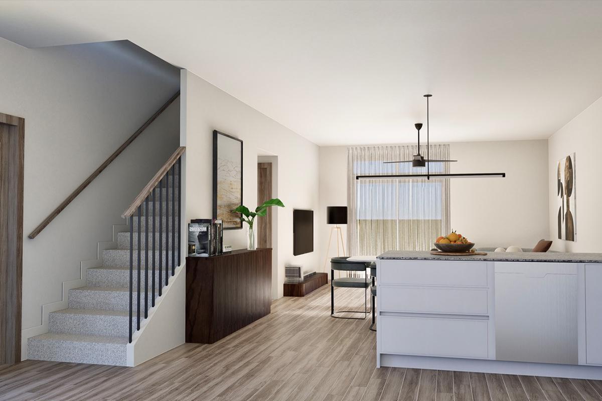 A modern kitchen and living area with a staircase on the left. The kitchen features a white island with a marble countertop and a fruit bowl. A dark wood sideboard is against the wall, with artwork and a lamp nearby. Natural light floods the room through a large window with sheer curtains.