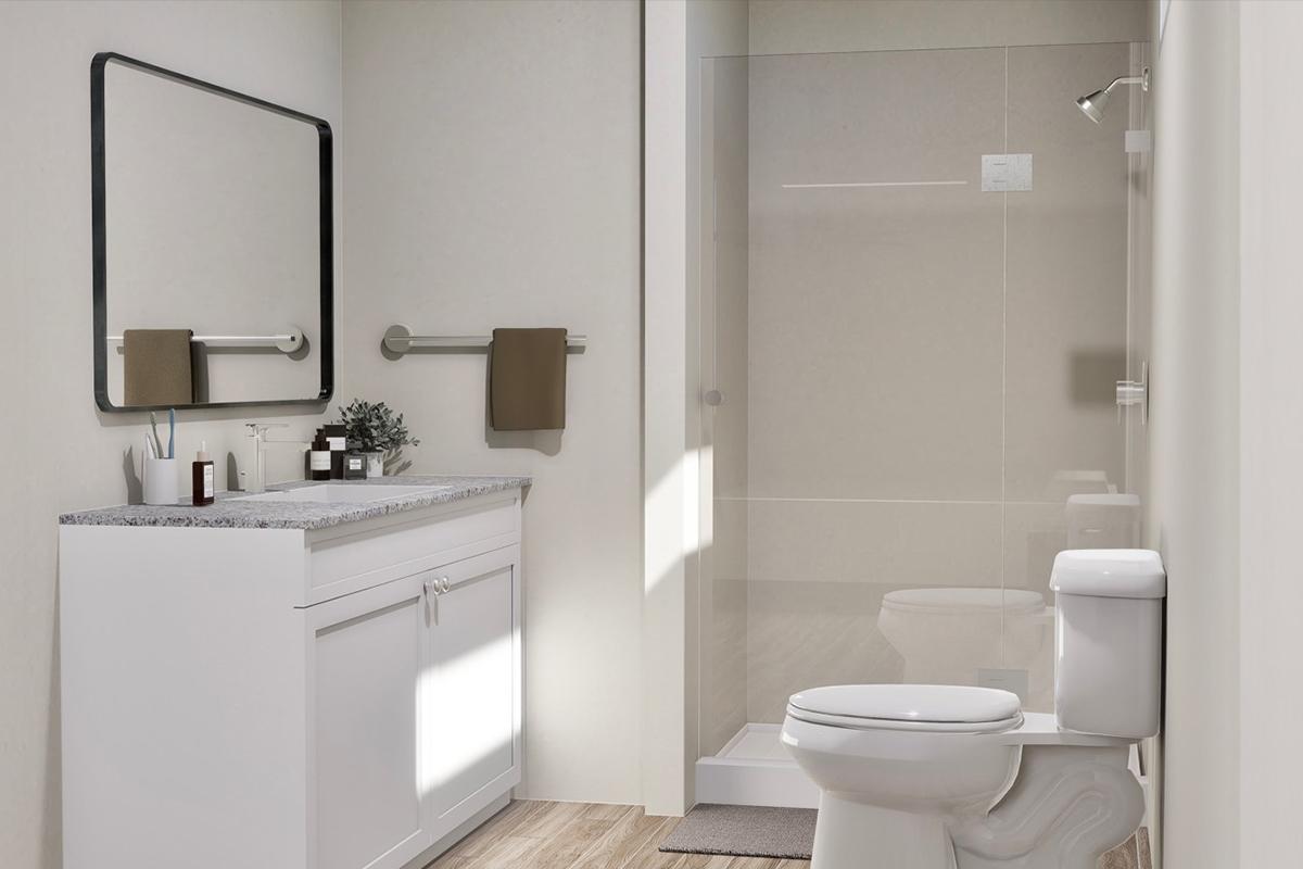 A modern bathroom featuring a white vanity with a granite countertop, a mirror, and toiletries. There's a glass shower on one side and a toilet on the other. Neutral-colored walls and wood-like flooring complement the space, with natural light illuminating the area.