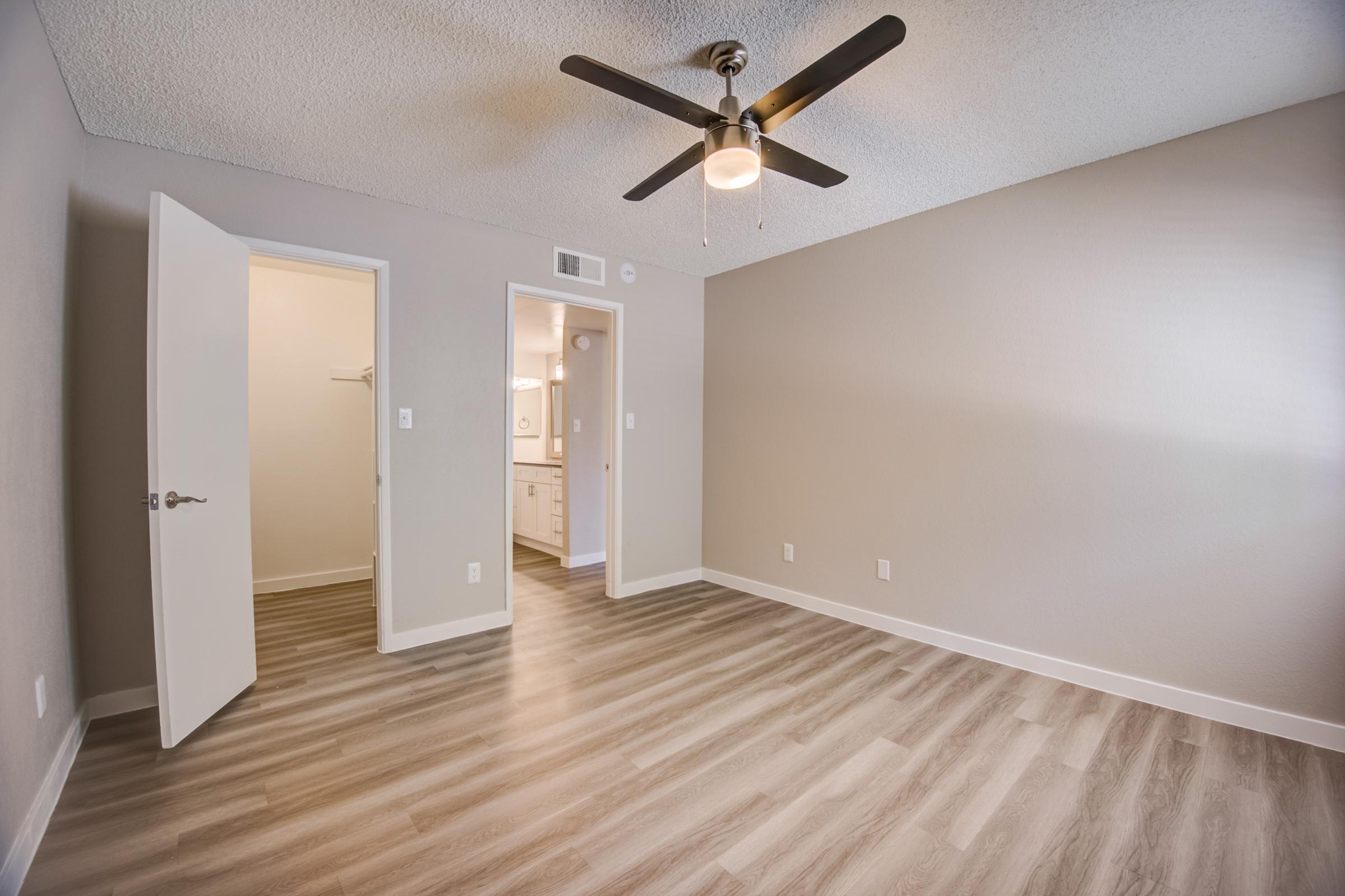 A bedroom with wood-style flooring, a ceiling fan and an ensuite bathroom at Rise at the Meadows.