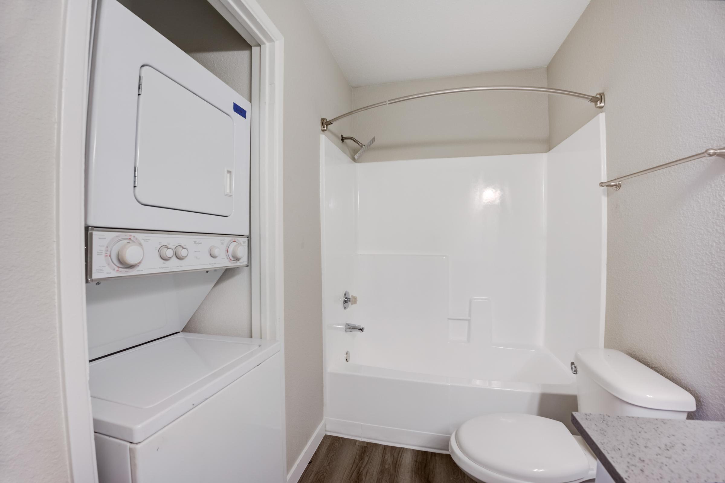 A bathroom with a tub and a washer and dryer at Rise at the Meadows.