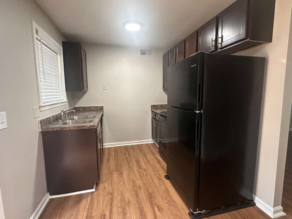 A modern kitchen featuring dark wood cabinetry, a black refrigerator, and stainless steel appliances. The countertops are a dark marble design, and the floor has a wood-like finish. Natural light enters through a window, providing a bright and inviting atmosphere.