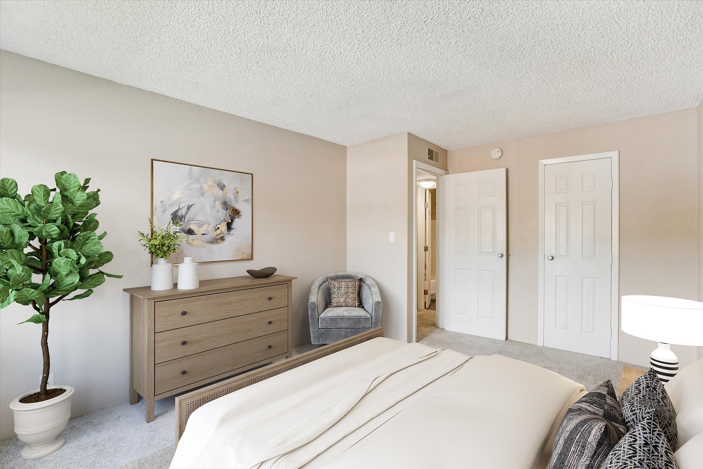 A cozy bedroom featuring a neutral color palette, a large painting above a wooden dresser, a potted plant in a corner, and a comfortable armchair. There are two closed doors in the background, and the room is softly lit, creating a warm and inviting atmosphere.