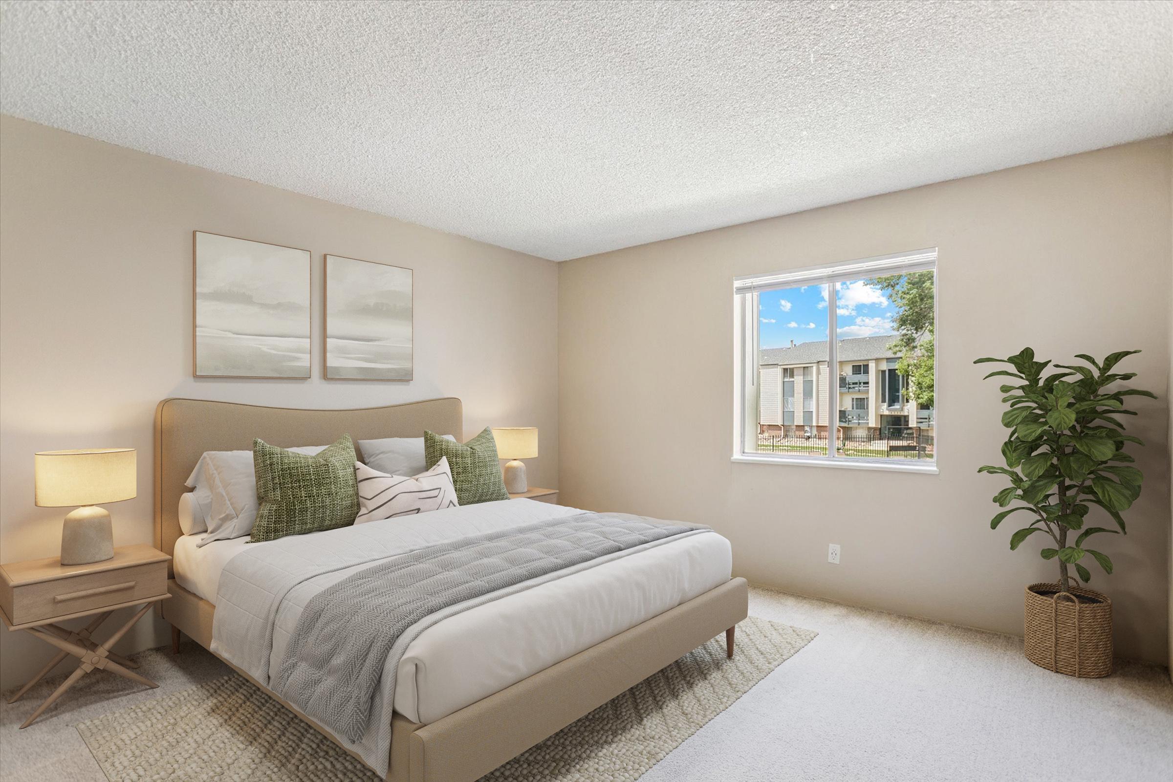 A cozy bedroom featuring a queen-sized bed with decorative pillows, two bedside lamps, and a neutral color scheme. There's a window with a view of exteriors, allowing natural light to enter, and a potted plant adds a touch of greenery to the space. Two framed art pieces hang above the bed.