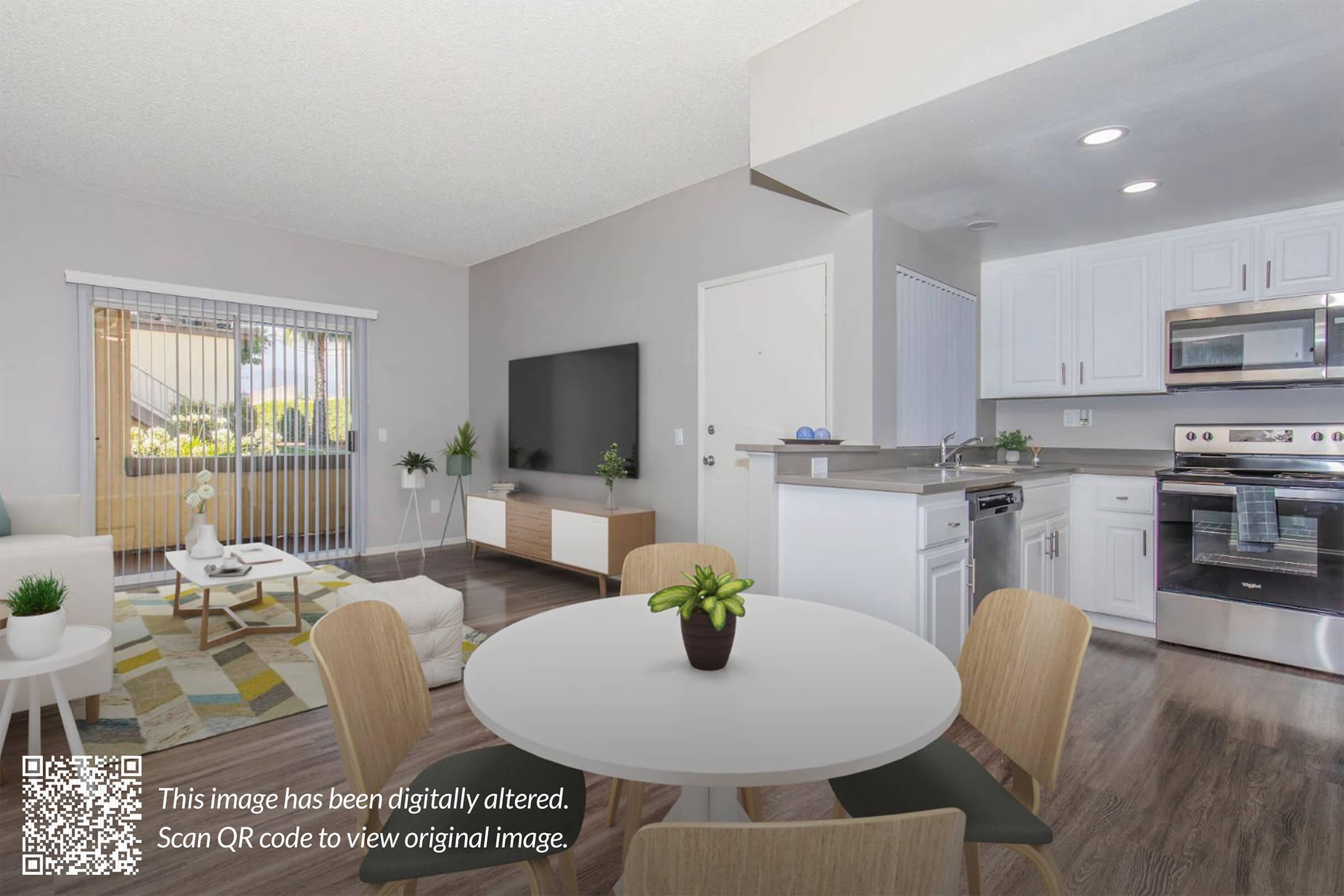 A modern, open-concept living space featuring a neutral color scheme. There is a cozy seating area with a sofa and a large TV, a dining table with four chairs, and a kitchen with white cabinets and stainless steel appliances. Natural light streams in from large windows, enhancing the bright atmosphere.