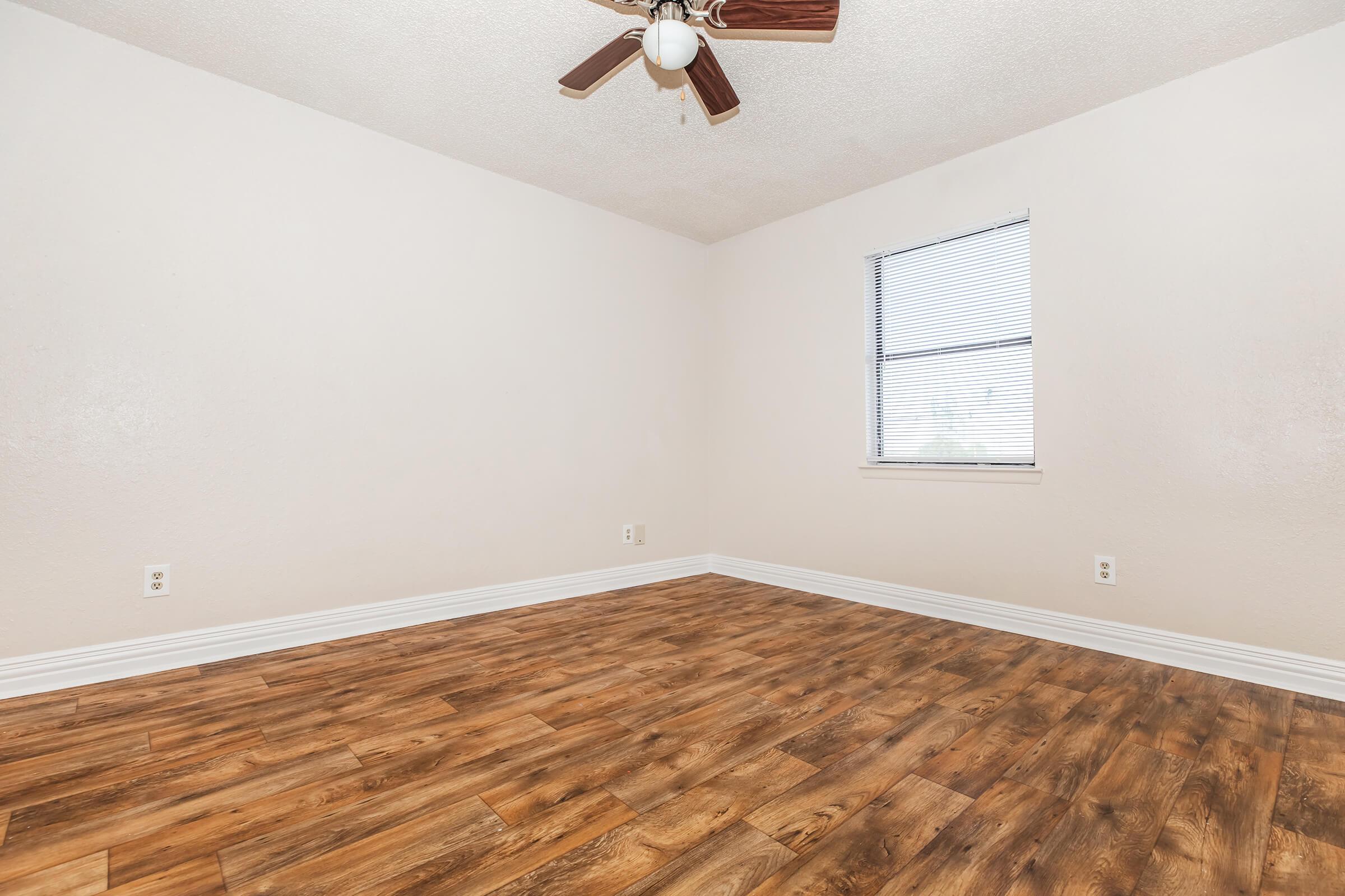 Empty room with light-colored walls, a ceiling fan, and a window featuring blinds. The floor is covered in wood laminate, and there are no furnishings or decorations present, creating a spacious and minimalist atmosphere.