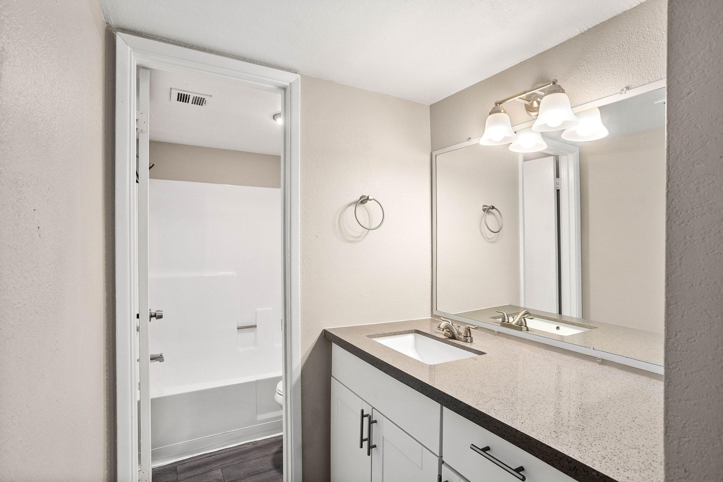 renovated bathroom with quartz countertops, white cabinets, and a large wall mirror