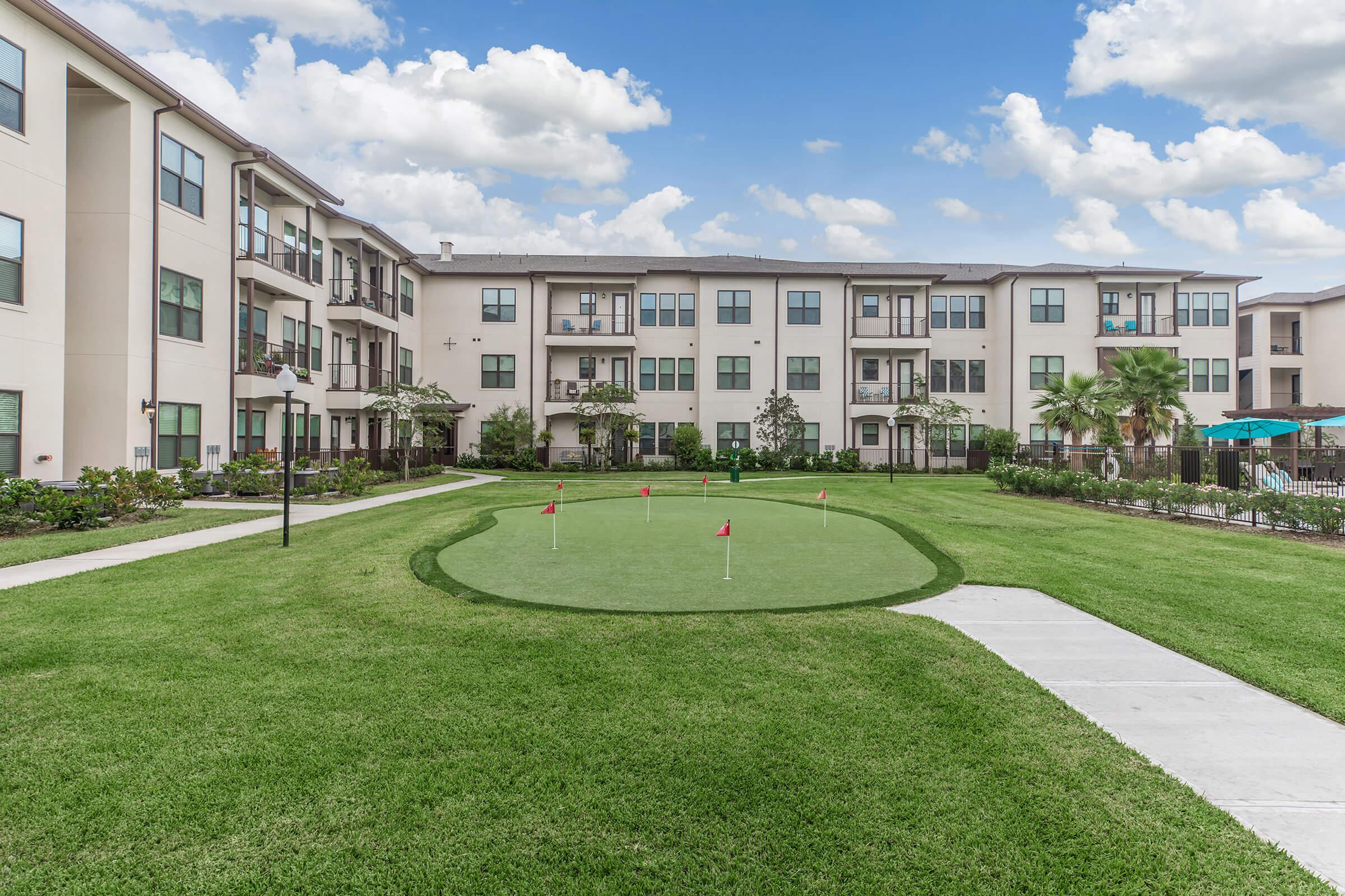 the grounds at ivy point kingwood senior living apartments featuring a putting green and view of the apartment exteriors