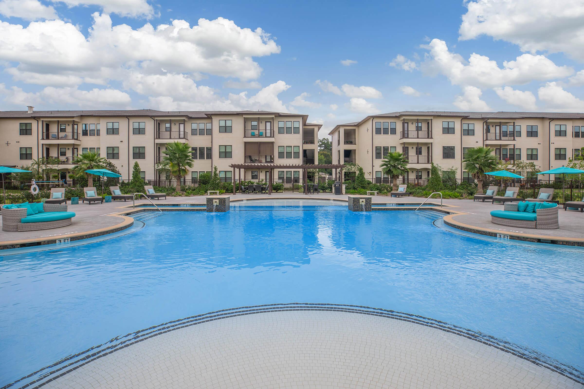 the pool area at ivy point kingwood senior living apartments featuring beach chairs and umbrellas