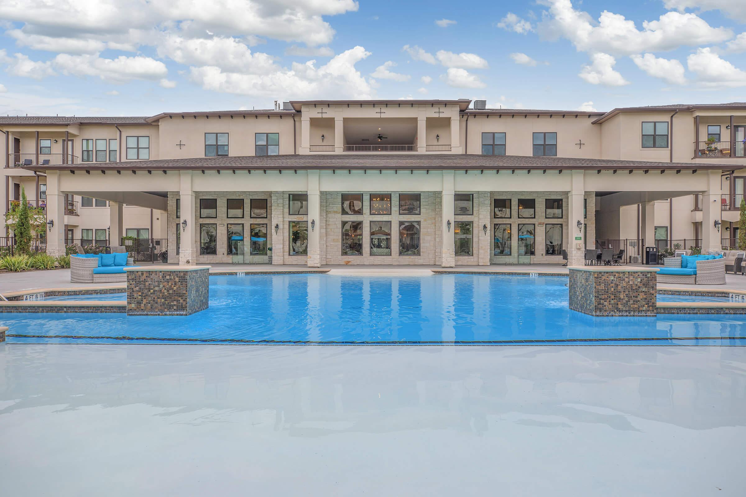 the pool area at ivy point kingwood senior living apartments featuring beach chairs and umbrellas