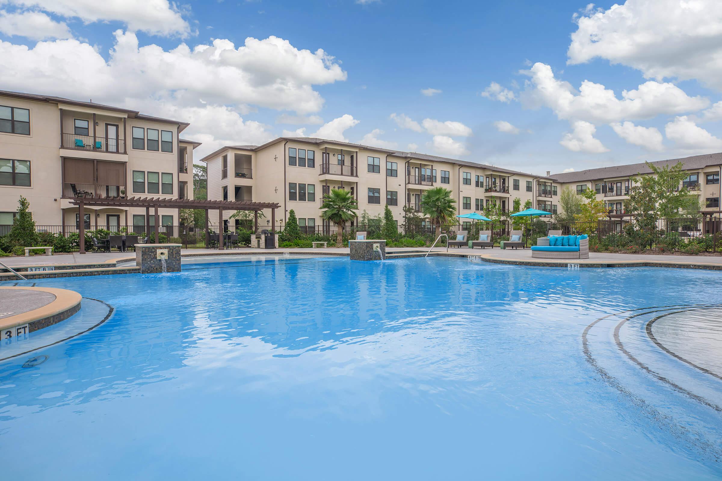 the pool area at ivy point kingwood senior living apartments featuring beach chairs and umbrellas