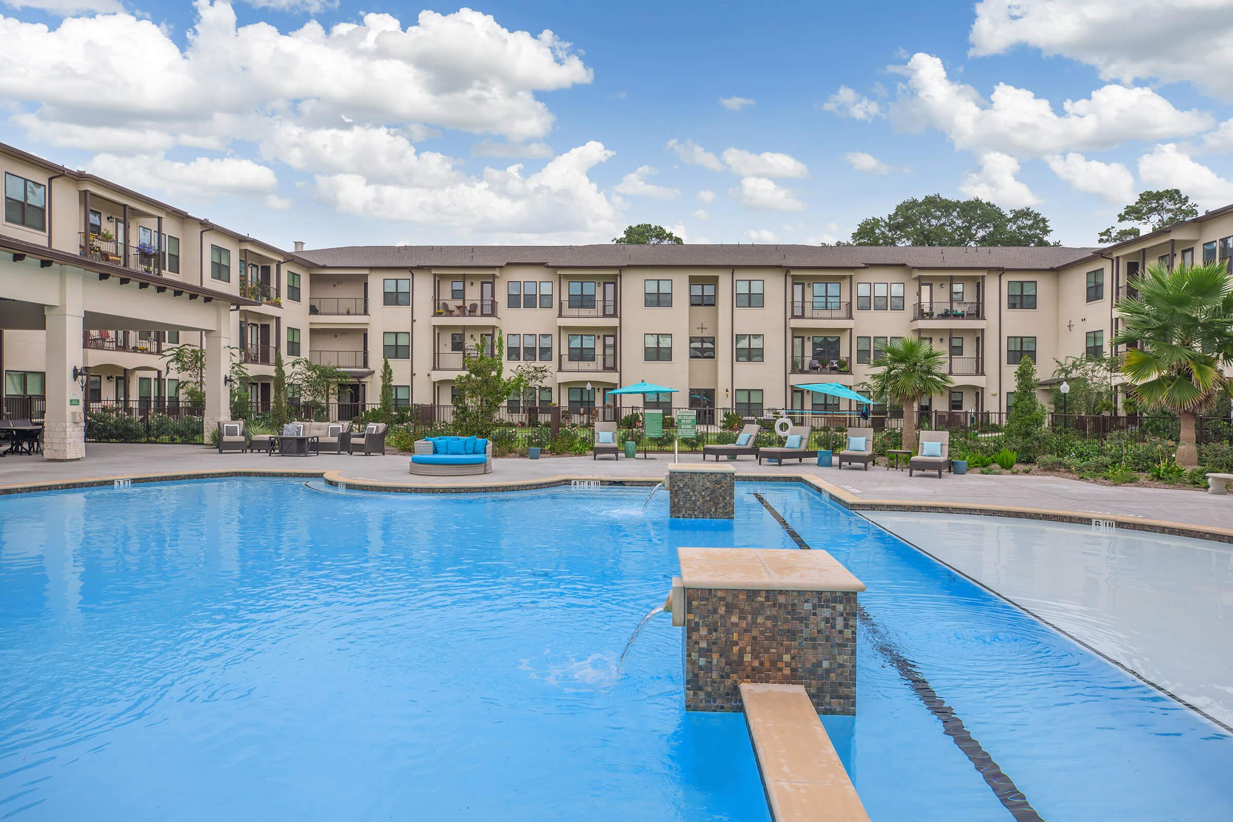 the pool area at ivy point kingwood senior living apartments featuring beach chairs and umbrellas