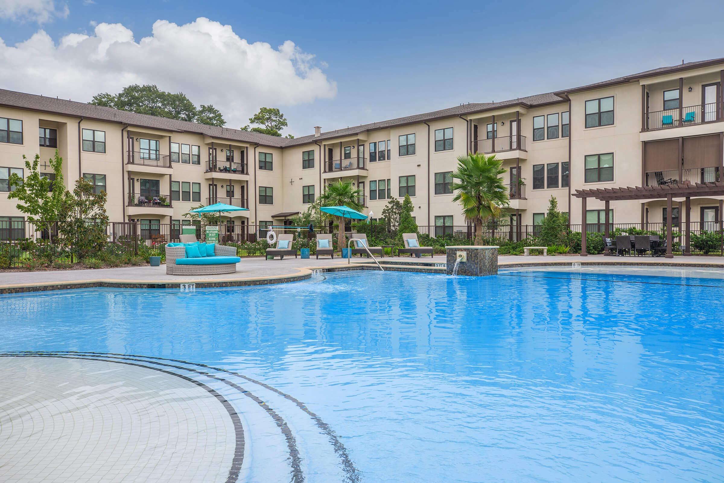 the pool area at ivy point kingwood senior living apartments featuring beach chairs and umbrellas