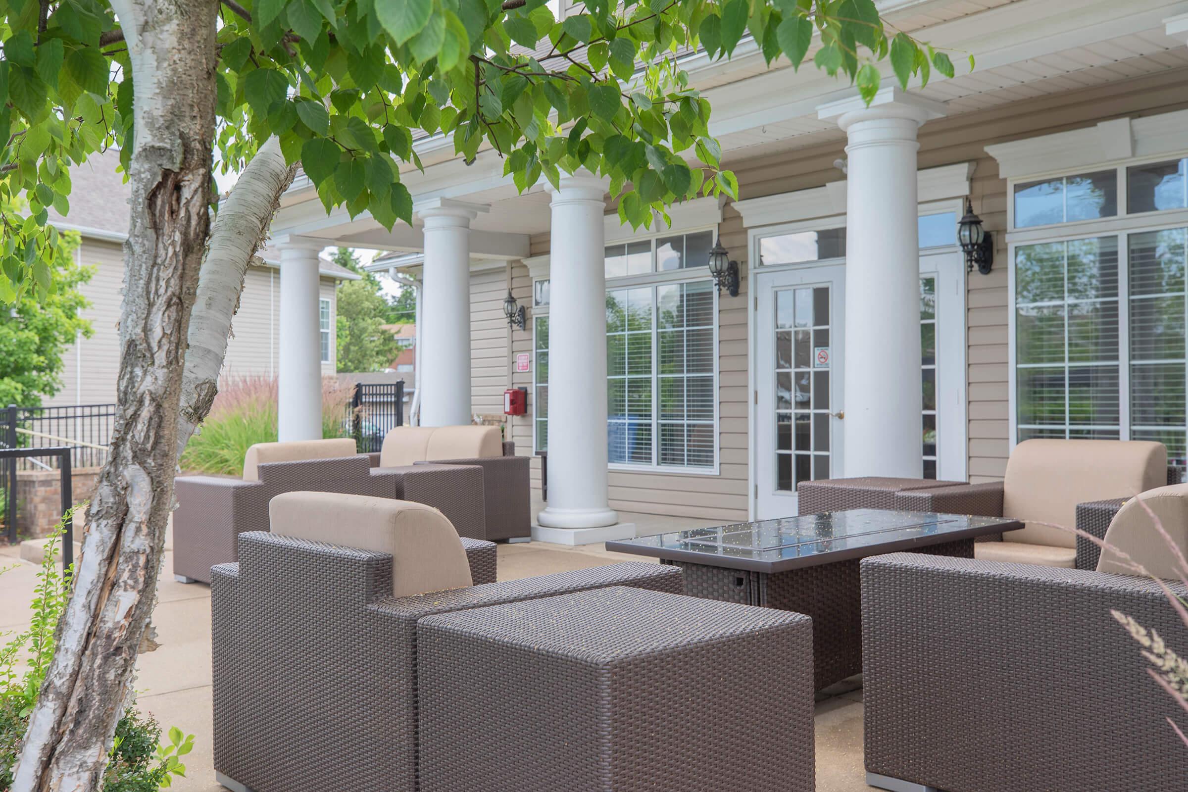 Outdoor seating area featuring a table with chairs, surrounded by greenery and columns, creating a cozy and inviting atmosphere.