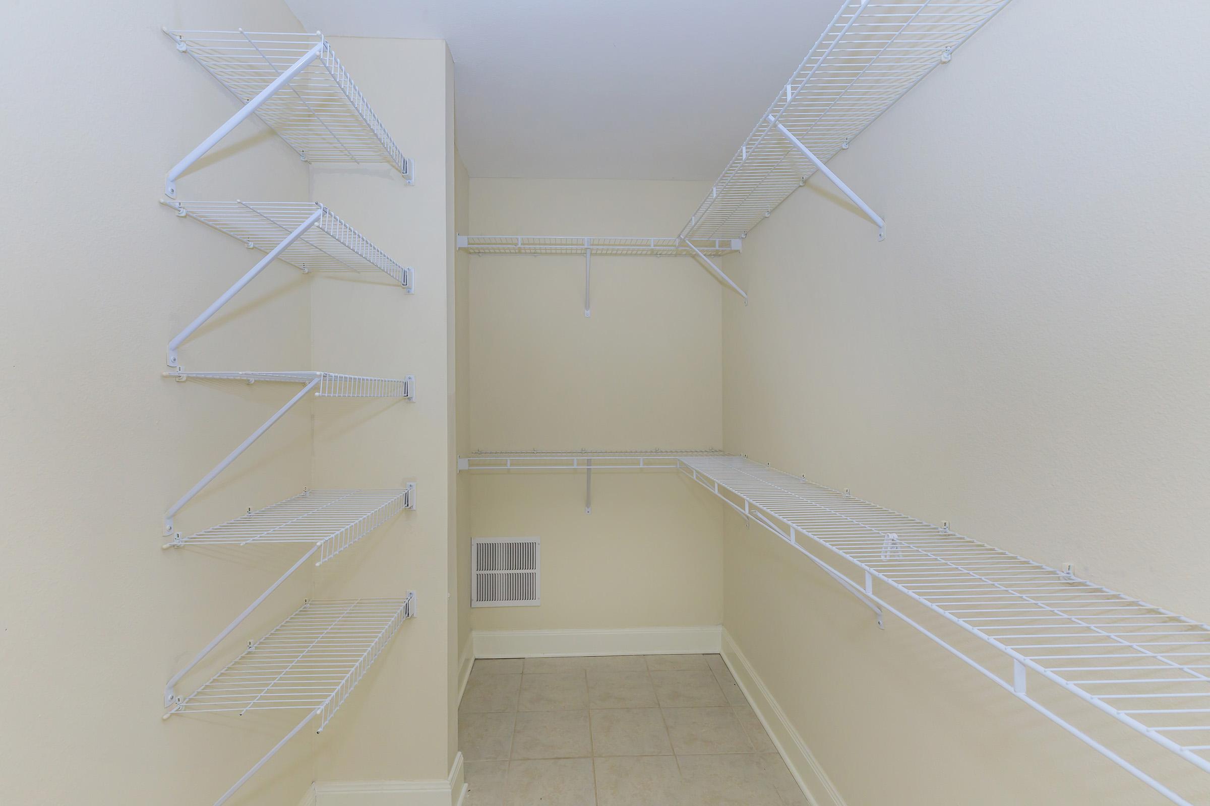 Empty walk-in closet featuring white wire shelving on three walls and a tiled floor. The walls are painted a light color, enhancing the bright and spacious feel of the area. No items are present, showcasing the shelving's organization potential.