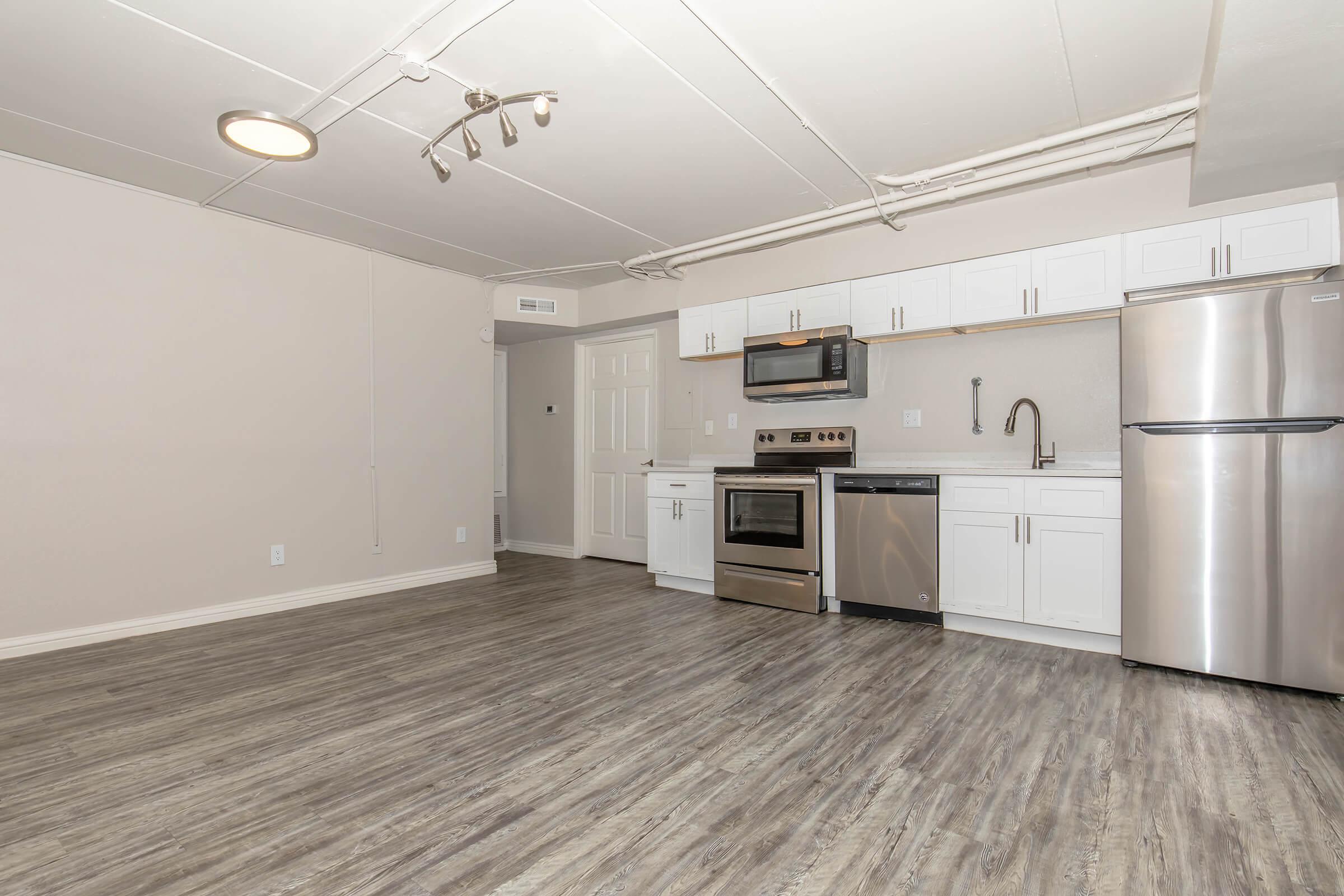 A neatly designed kitchen with stainless steel appliances, including a microwave, oven, and refrigerator. The space features white cabinetry, a sink with a modern faucet, and a stylish hardwood floor. Soft overhead lighting illuminates the room, creating a warm, inviting atmosphere.