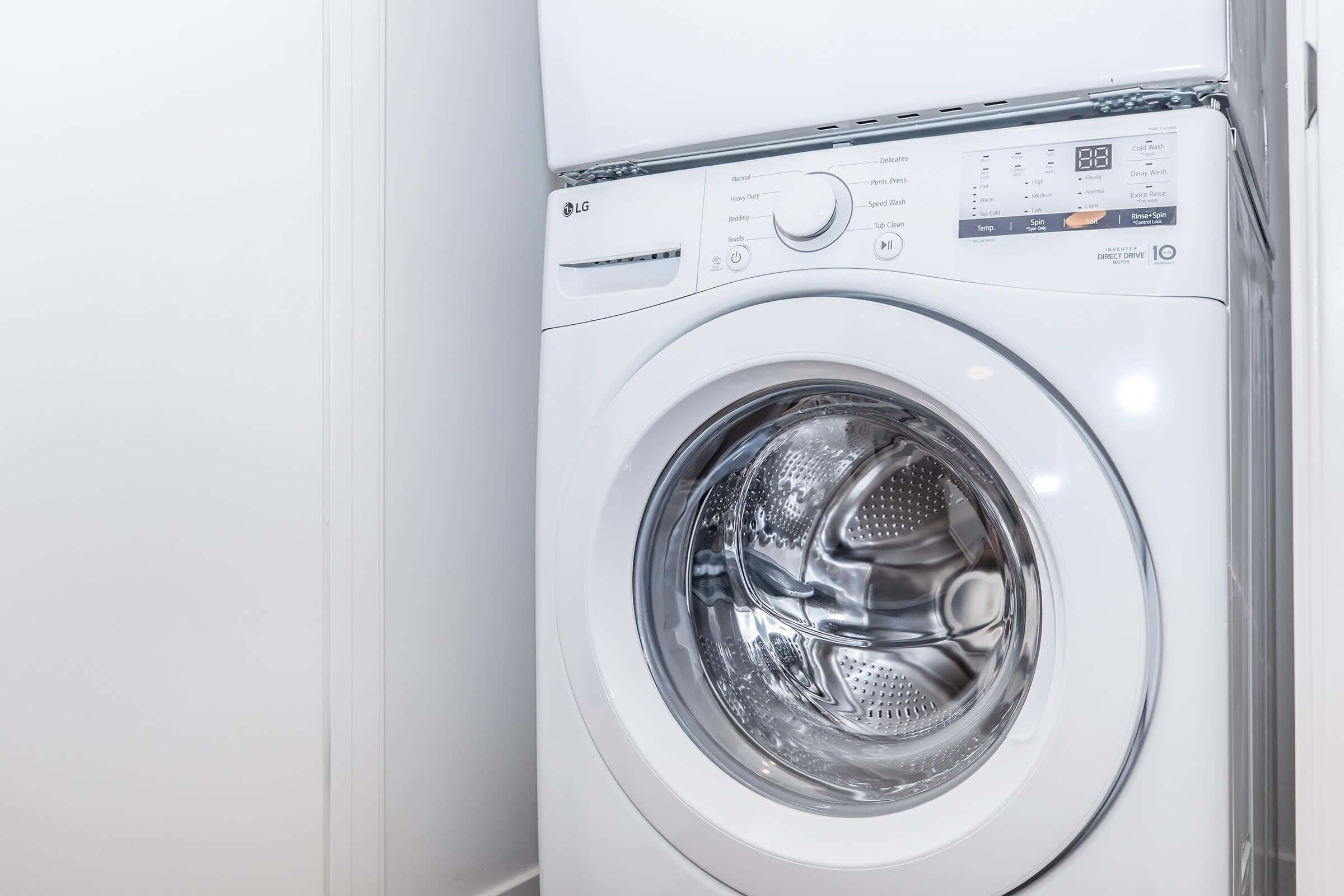A modern LG washing machine in a bright laundry room. The washer features a transparent door, control panel with buttons, and is positioned near a wall, showcasing a clean and minimalist design.