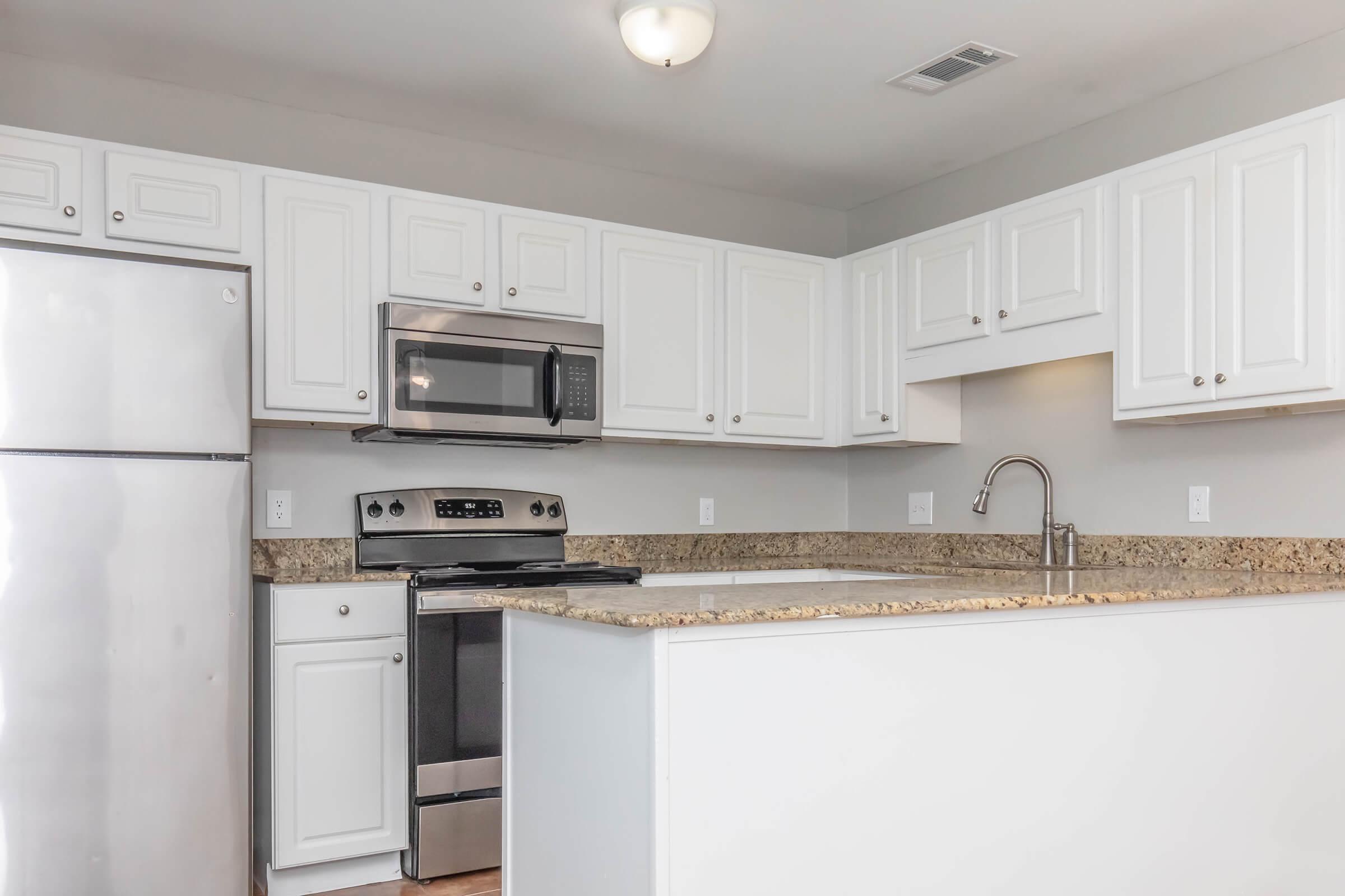 Modern kitchen featuring white cabinets, stainless steel appliances, a silver refrigerator, a microwave above the stove, and a granite countertop. The design is sleek and contemporary, with a bright, neutral color scheme.