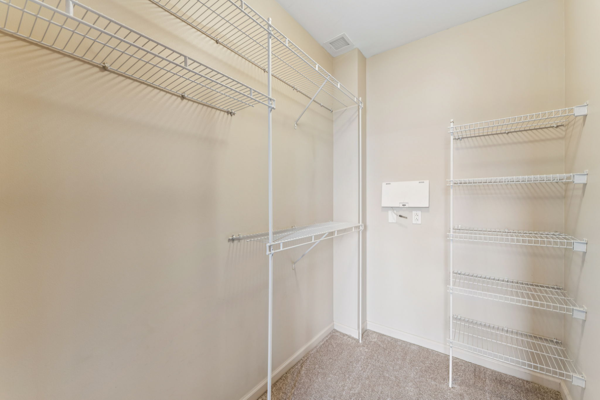 A spacious, empty closet featuring metal wire shelving on two sides. The walls are painted a light color, and the floor is carpeted. There's a white mail organizer mounted on the wall, and the setting is bright and uncluttered, creating an inviting storage space.