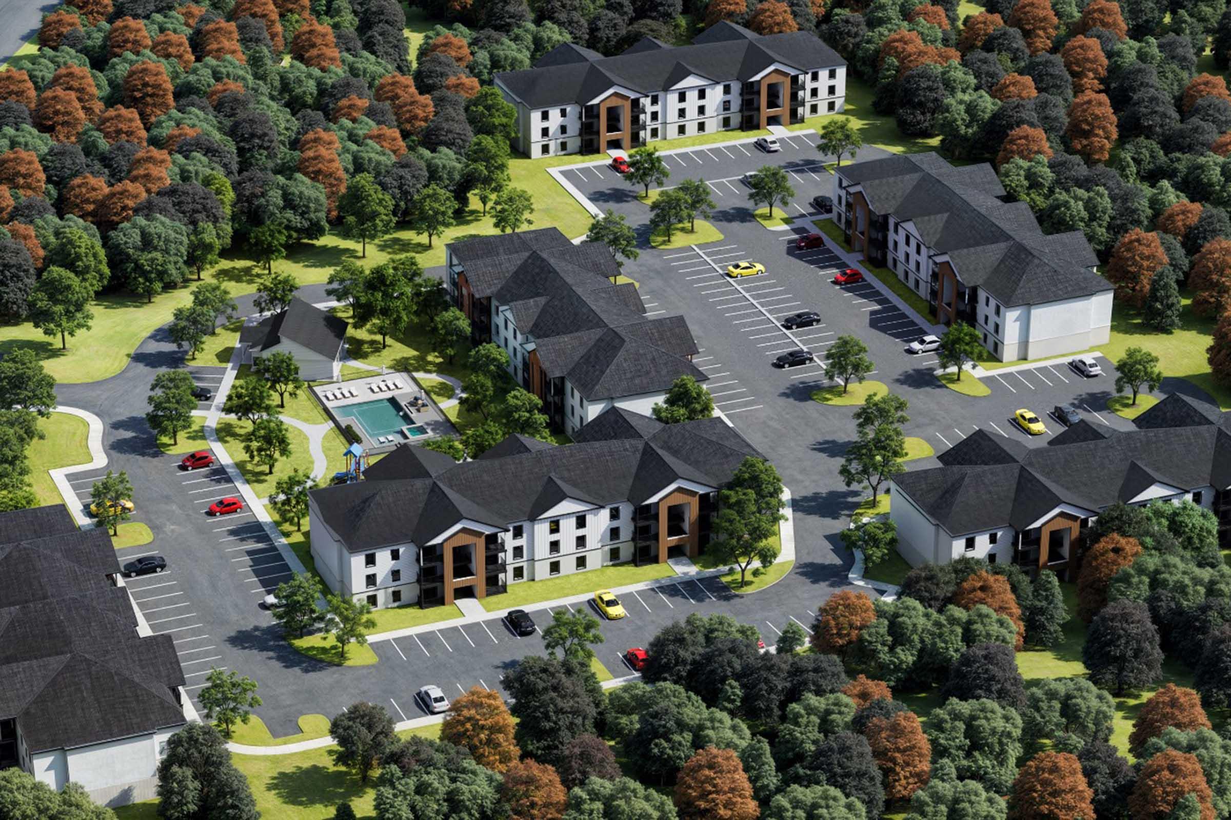 Aerial view of a residential complex featuring multiple buildings with modern architecture. The layout includes several parking lots, green spaces with trees, and a swimming pool area. The surrounding landscape is filled with trees displaying autumn colors, creating a vibrant atmosphere.