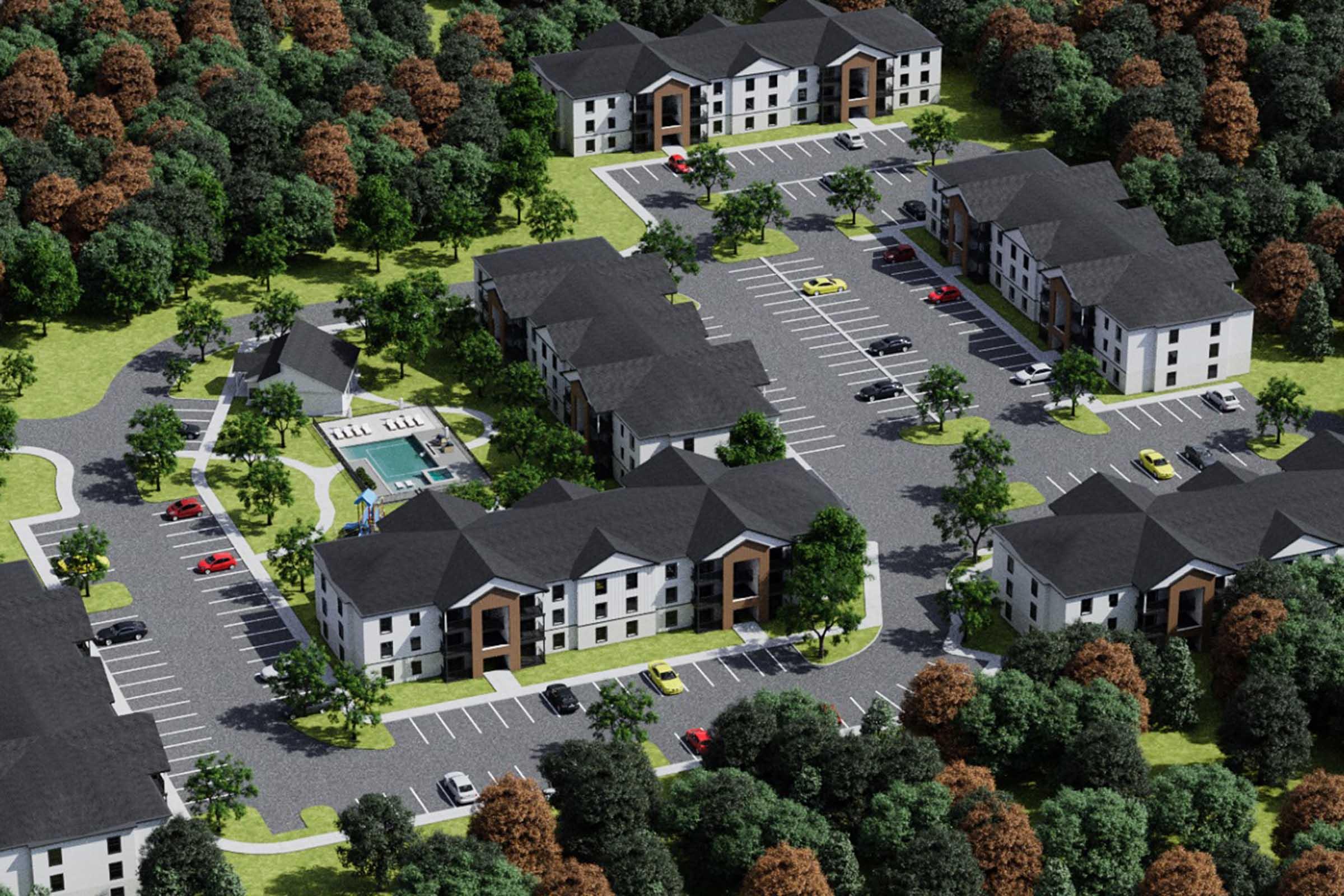 Aerial view of a residential complex featuring multiple buildings with a contemporary design. Surrounding green landscape with trees in varying shades, a parking lot filled with cars, and a swimming pool area is visible in the center of the complex.