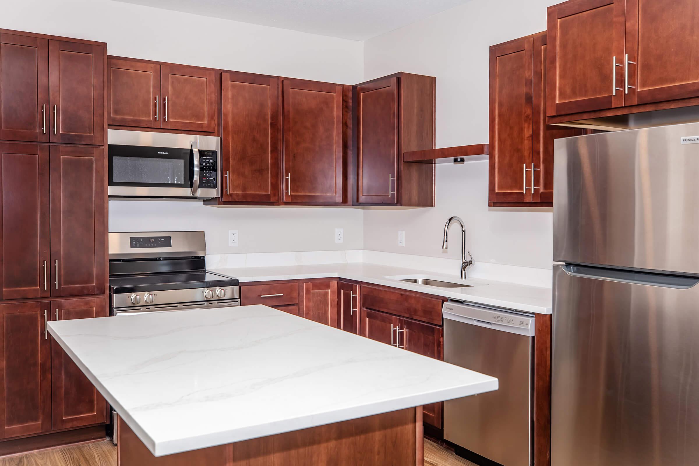 Modern kitchen featuring dark wood cabinetry, stainless steel appliances including a microwave and dishwasher, a sleek countertop with an island, and a spacious layout. The design combines functionality and style, perfect for cooking and entertaining.