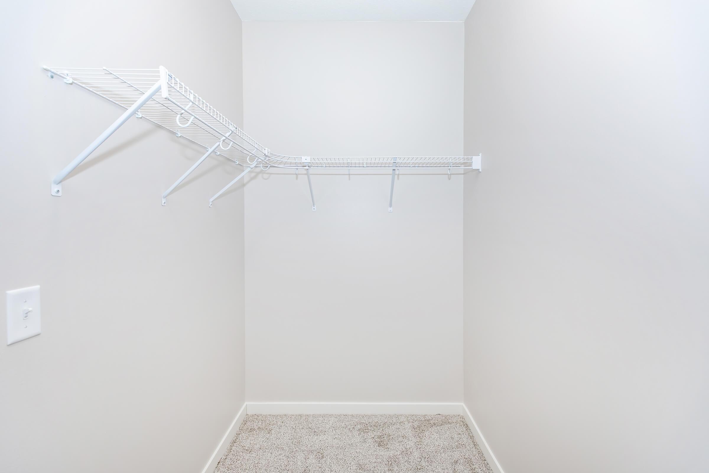Empty closet with a white wire shelving unit attached to the wall. The walls are painted a light color, and the floor is covered in a beige carpet. There are no items or clothing present, creating a minimal and uncluttered appearance.