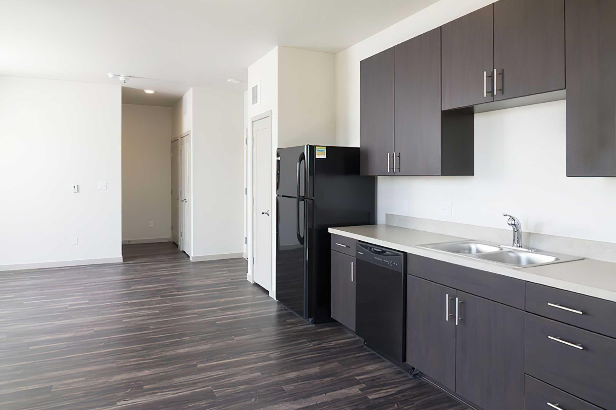 Modern kitchen with dark wood cabinets, stainless steel sink, and black appliances including a refrigerator and dishwasher.