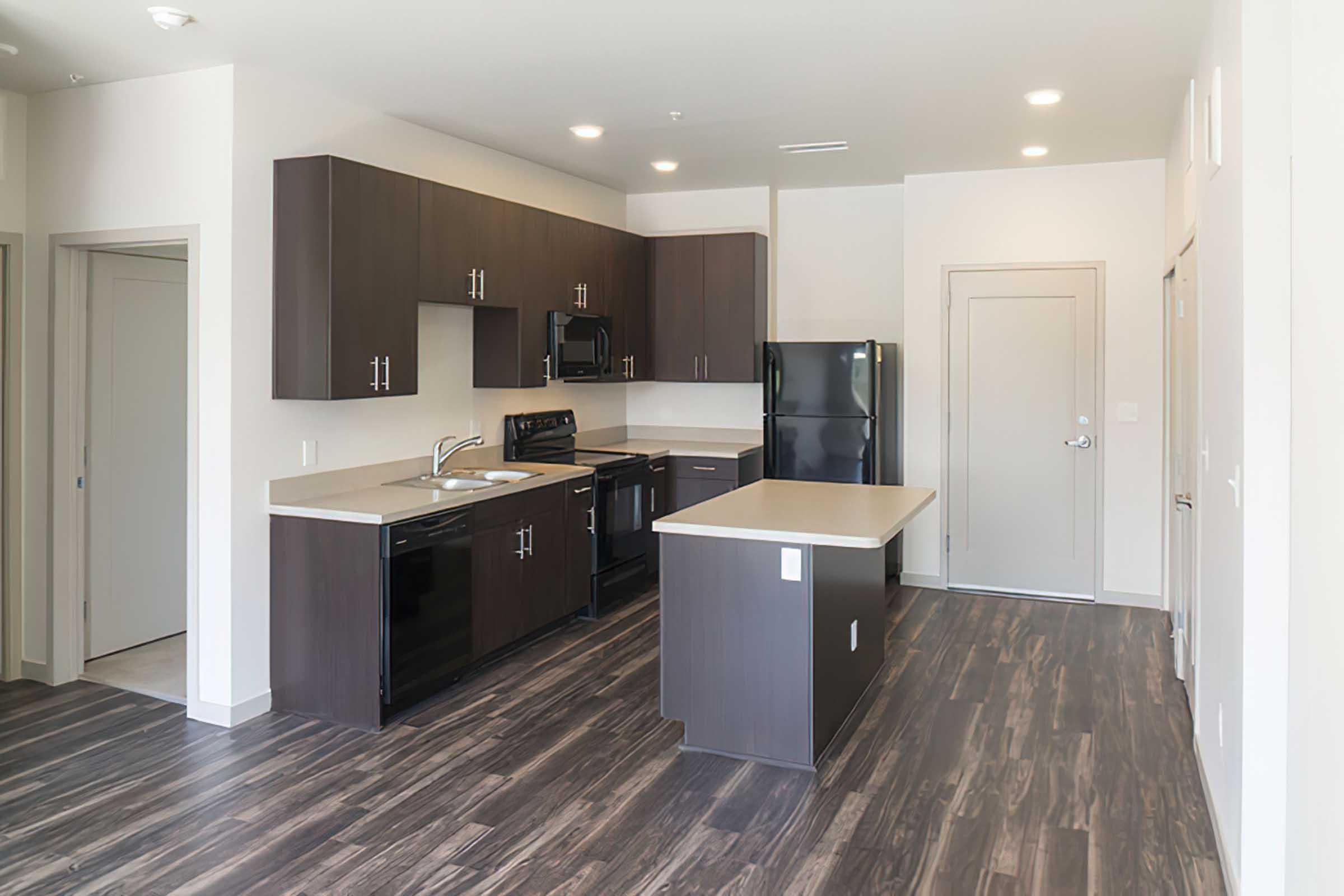 Modern kitchen featuring dark wood cabinetry, black appliances, and a central island with a countertop.