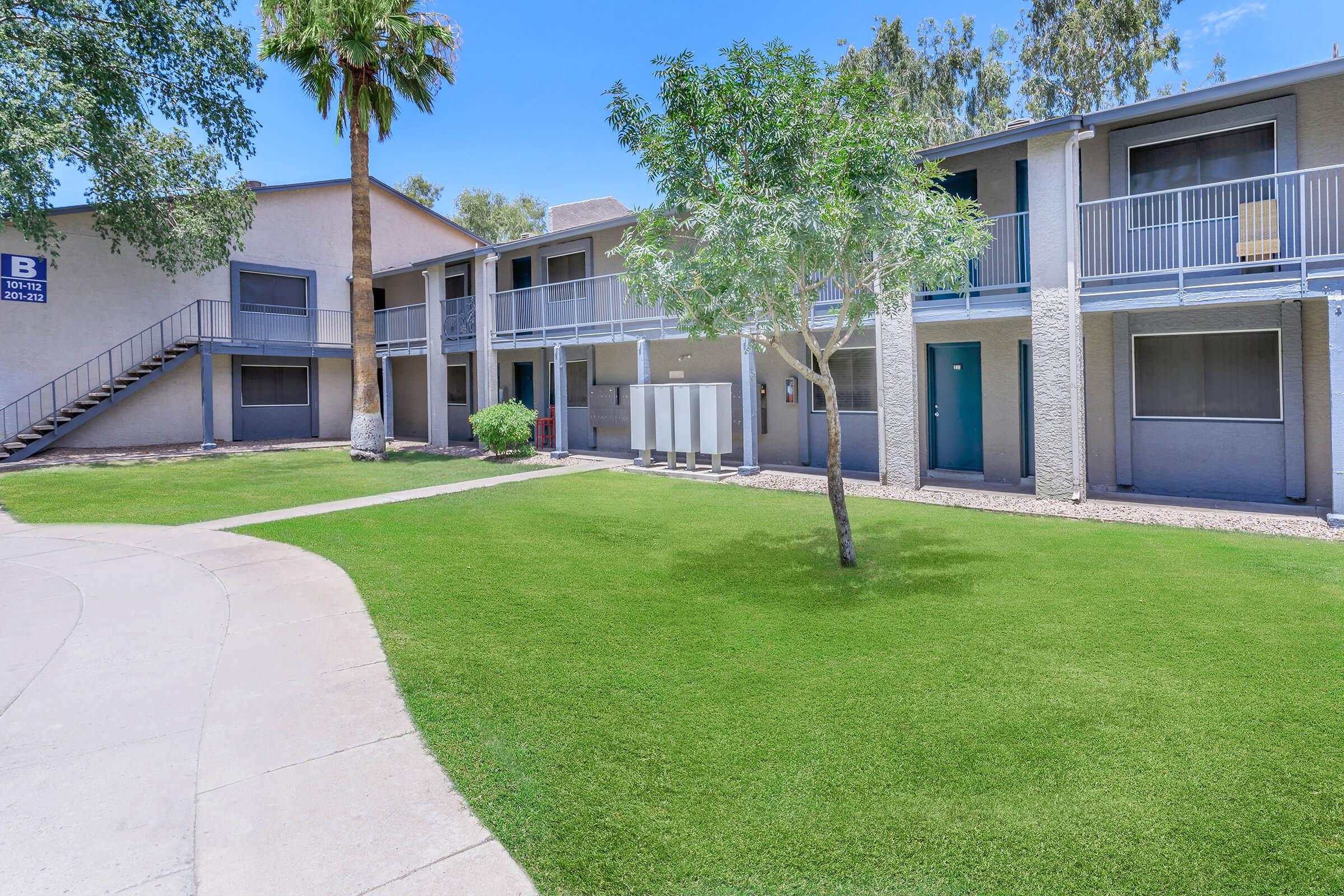 Rise on Cave Creek's two-story apartment building with large grassy lot and trees in front 
