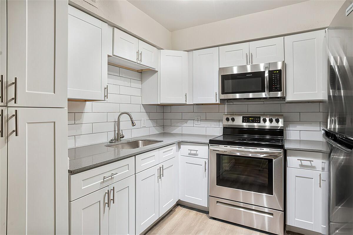 Modern renovated kitchen with white cabinets, stainless steel appliances, and grey quartz countertop