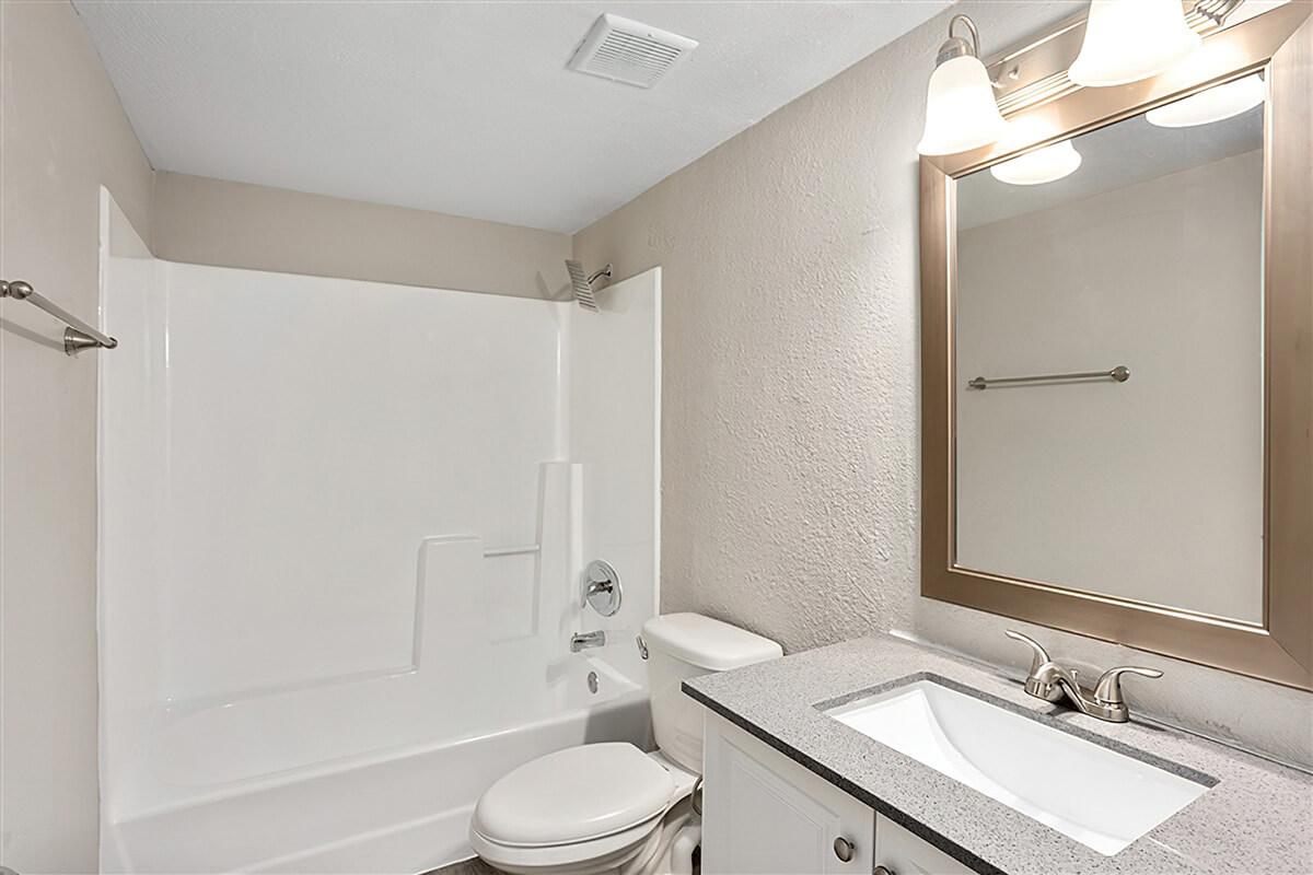 Modern bathroom with mirror sink vanity, toilet, and white tile shower