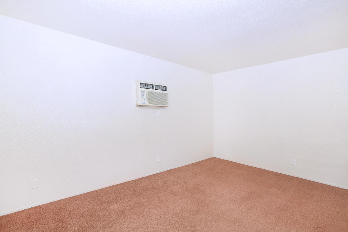 Empty room with light-colored walls and carpeted floor. An air conditioning unit is mounted on one wall. There are no furniture or decorations present, creating a spacious and minimalist appearance.