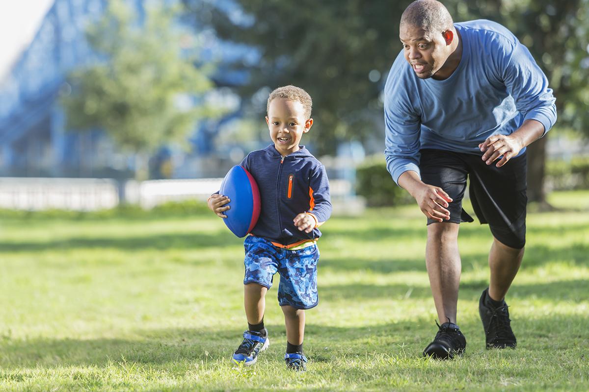 a young boy holding a football ball on a field playing frisbee