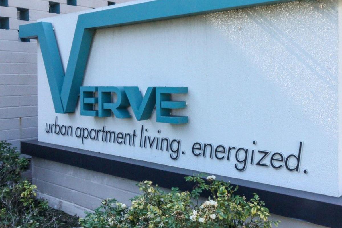 Sign for "VERVE" with the tagline "urban apartment living. energized." The sign features a modern design and a combination of bold and sleek typography, set against a light background with a landscaped area below.