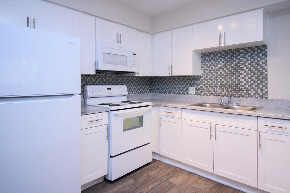 Modern kitchen featuring white cabinets, a stainless steel microwave, an electric stove, and a refrigerator. The countertop is grey with a tiled backsplash of small mosaic patterns. The space is clean and well-lit, showcasing a contemporary design.