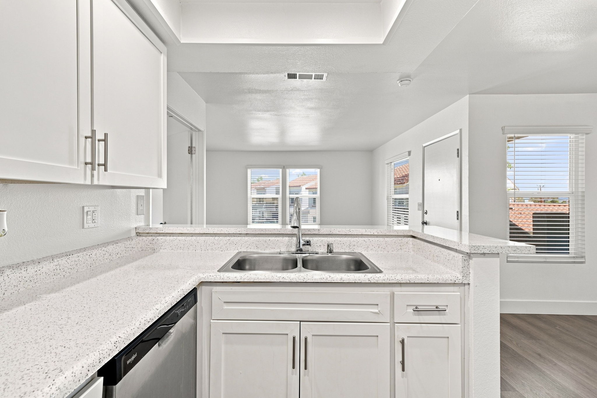 Modern kitchen with white cabinetry, a double sink, and a countertop featuring a speckled design. Stainless steel appliances and large windows allow natural light to brighten the space, creating a clean and inviting atmosphere.