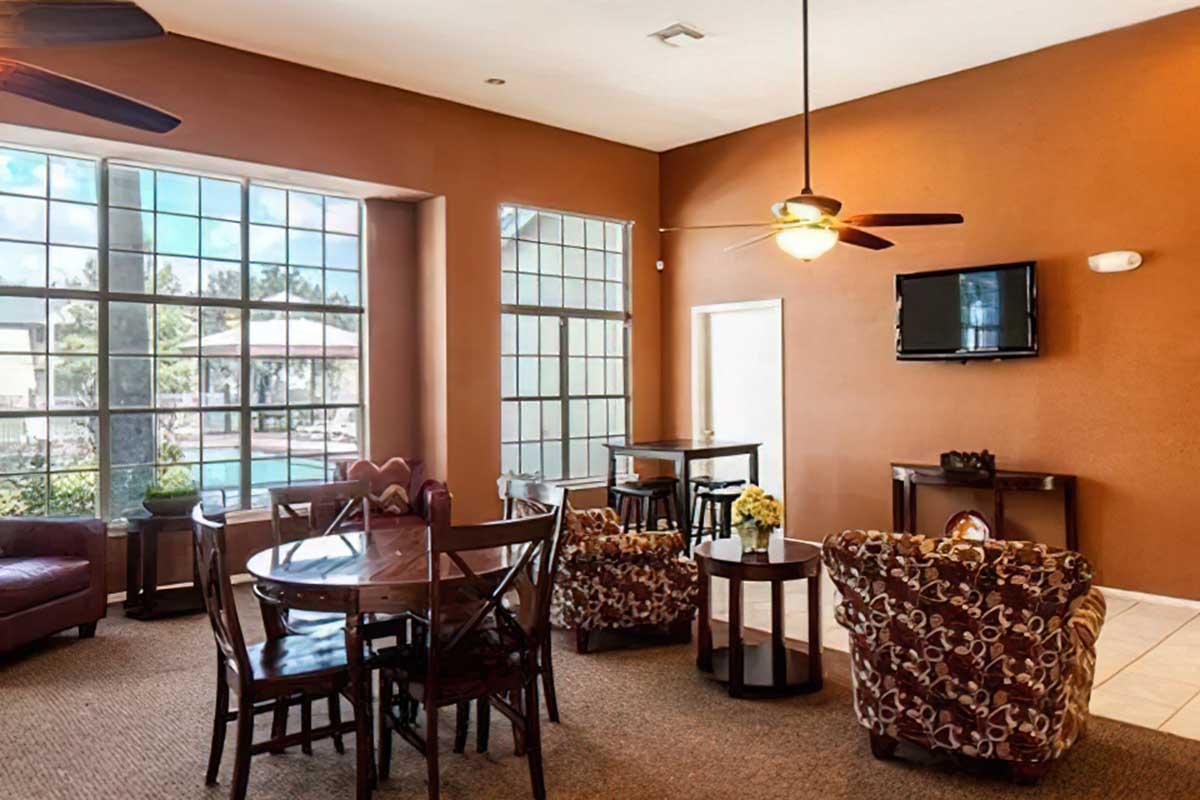 Interior of a cozy lounge area featuring comfortable seating, a table with four chairs, ceiling fans, and large windows that let in natural light.