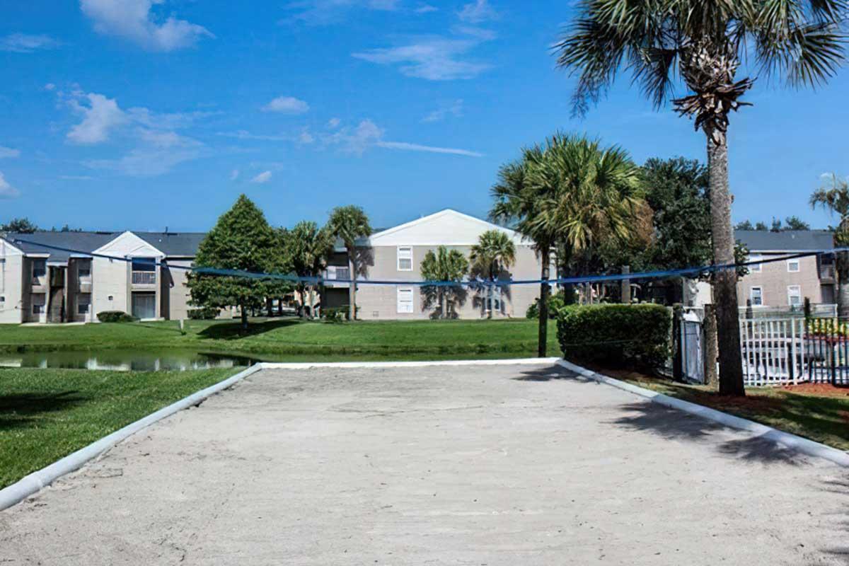 A sand volleyball court in a landscaped area surrounded by palm trees and grass.
