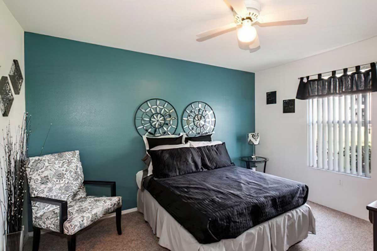 A cozy bedroom featuring a black bedspread, decorative black and silver wall art, and a teal accent wall.